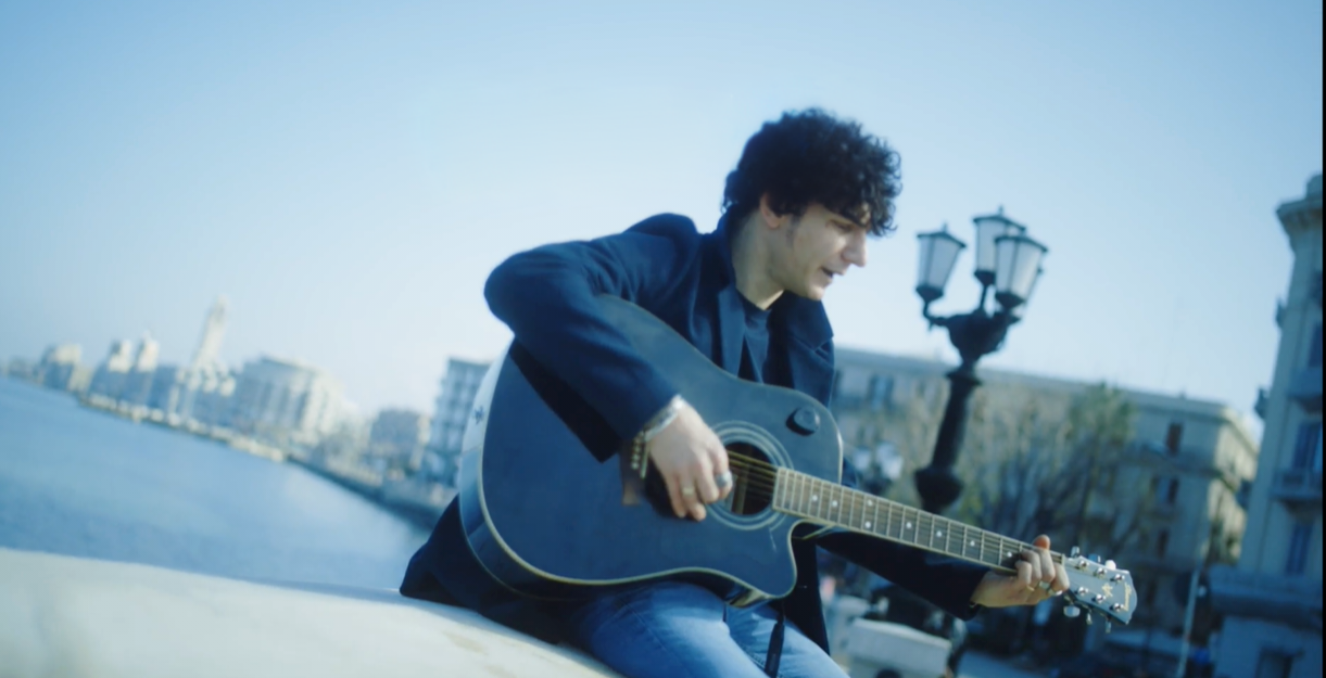 Cantante Piergiorgio Corallo con chitarra suona su un muretto del lungomare di Bari