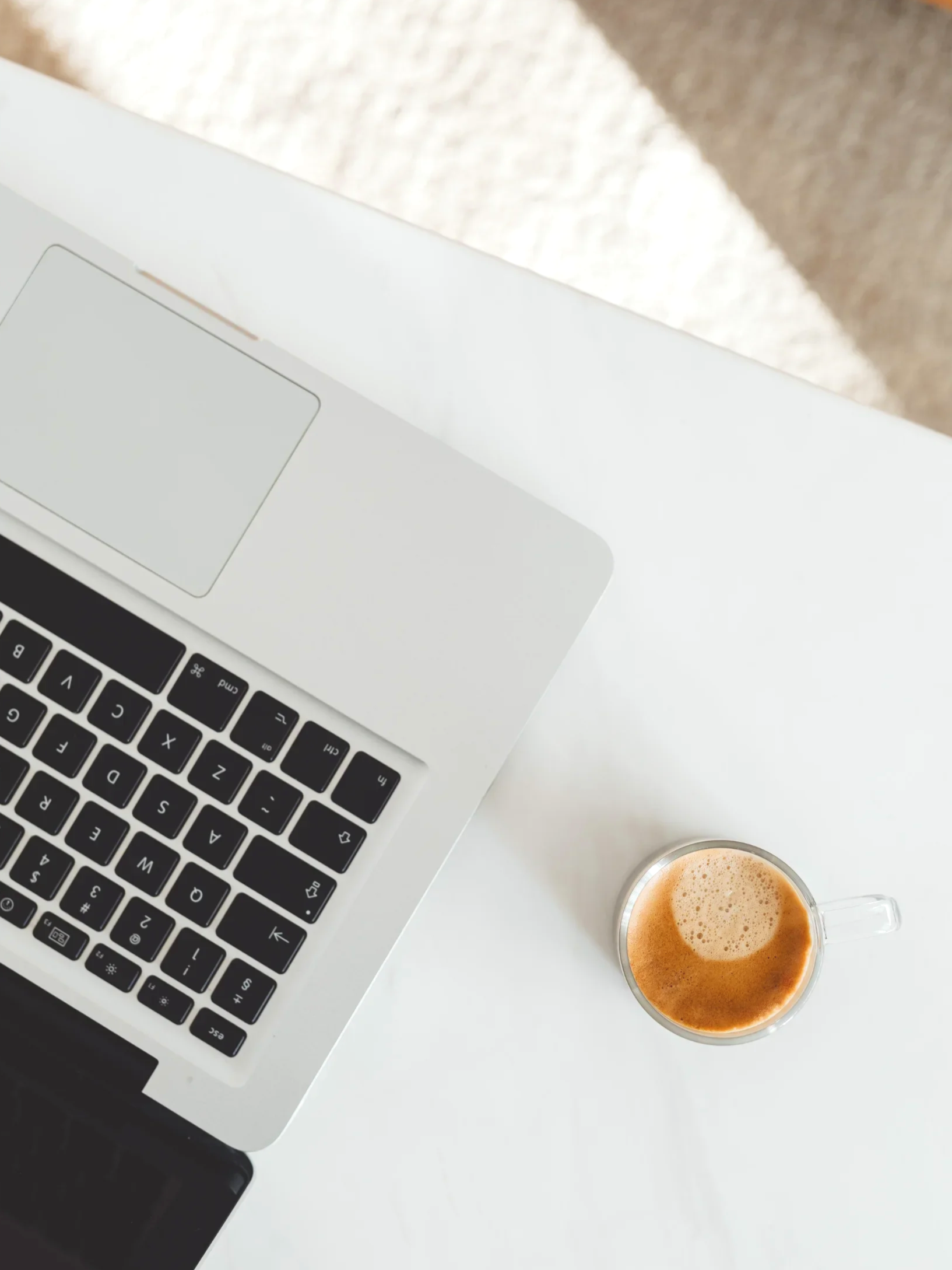 Ein Laptop, eine Tasse Kaffee und ein Smartphone auf einem weißen Tisch.