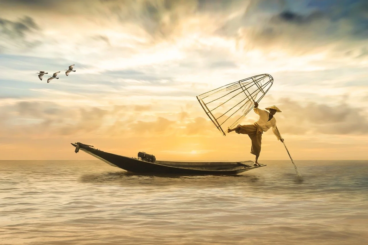 Ein Mensch steht auf einem Boot im Meer bei Sonnenuntergang, trägt traditionelle Kleidung und hält einen großen Korb in der Hand, während Gänse im Himmel fliegen.