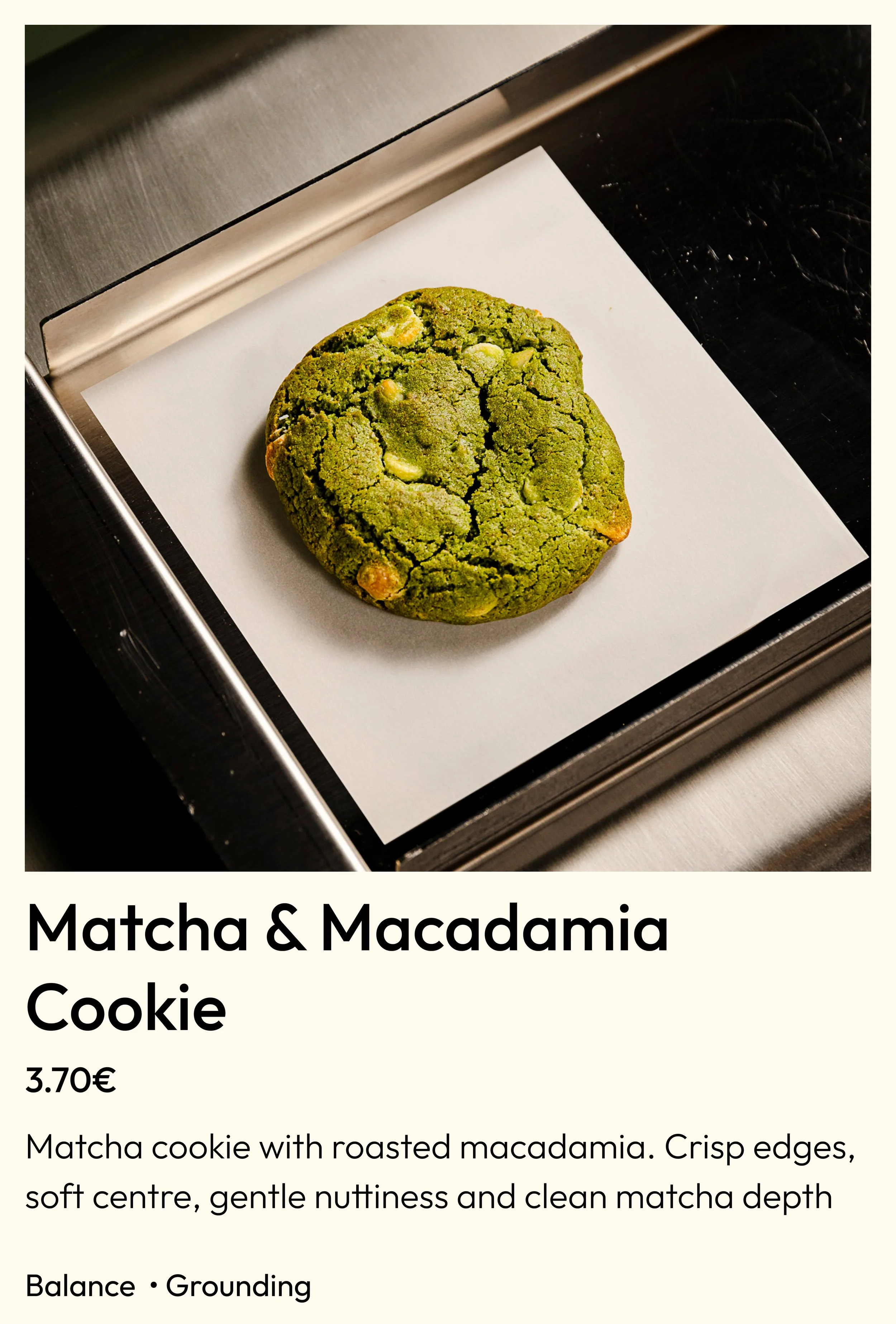 A matcha and macadamia cookie on a white paper sheet on a metal tray.