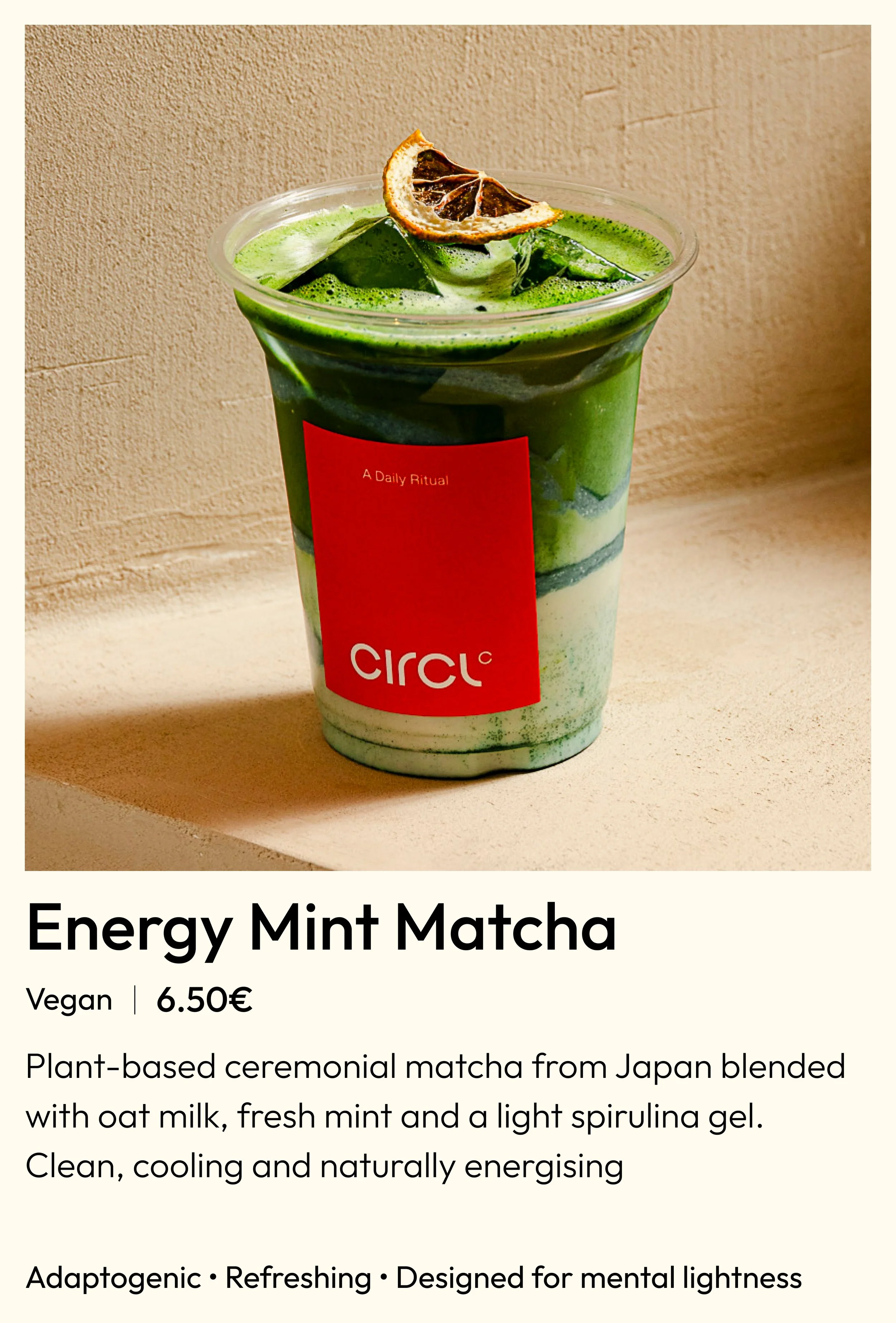 A plastic cup filled with green matcha latte topped with a dried lemon slice garnish and ice cubes. The cup has a red label with the word 'Circuit' on it.