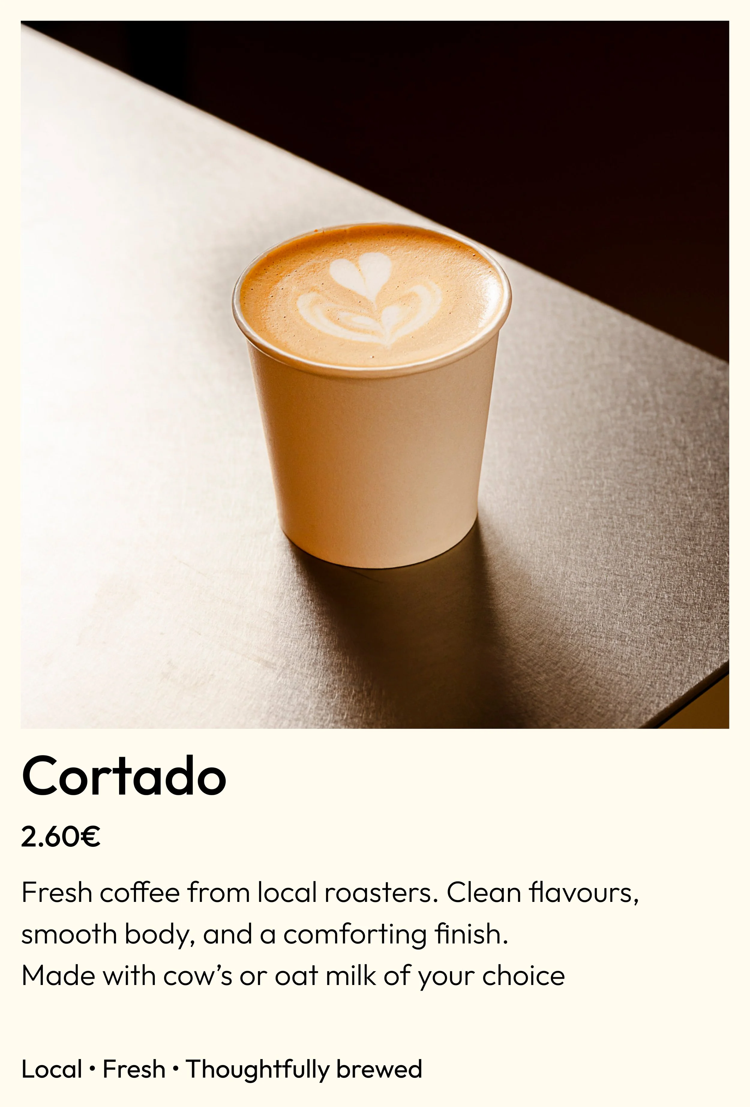 A white paper cup filled with a latte featuring a heart-shaped latte art design on top, placed on a dark surface with a background that is dark on the top right.