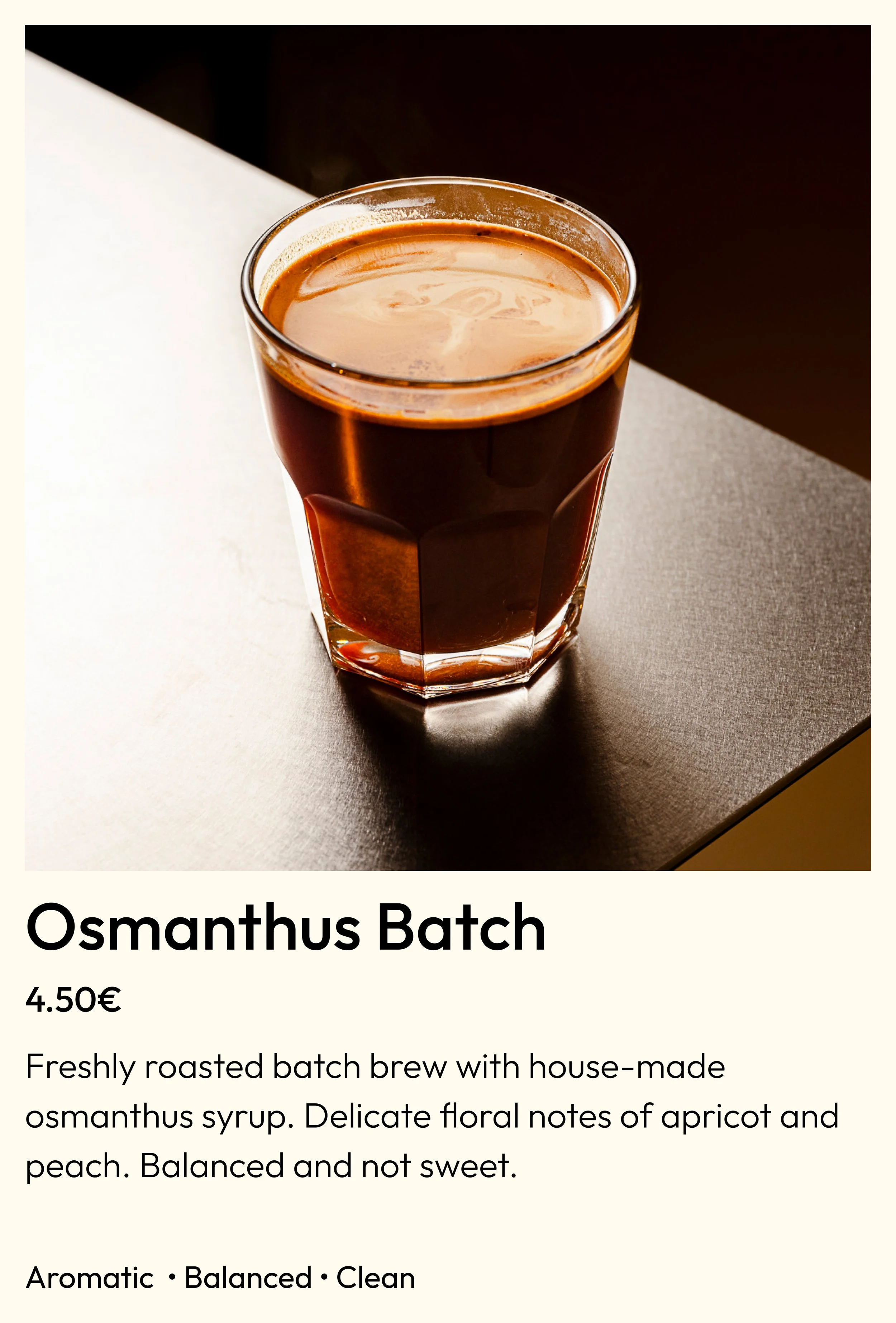 A glass of freshly brewed Osmanthus Batch coffee with a rich, dark color, placed on a dark tabletop with light coming from the top left.