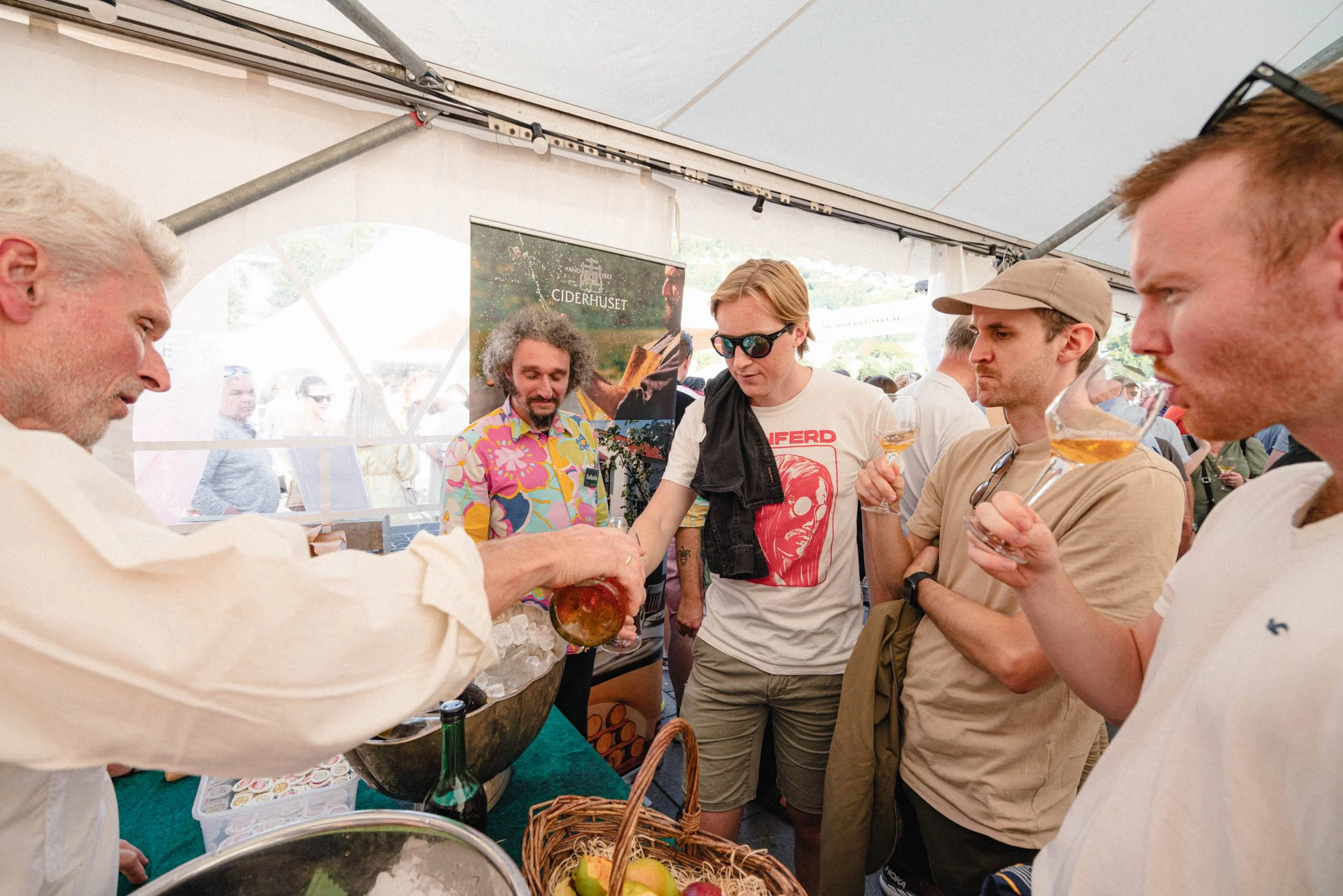 Mann som pomser en drikkekopp til en gruppe mennesker under en utendørs festival.