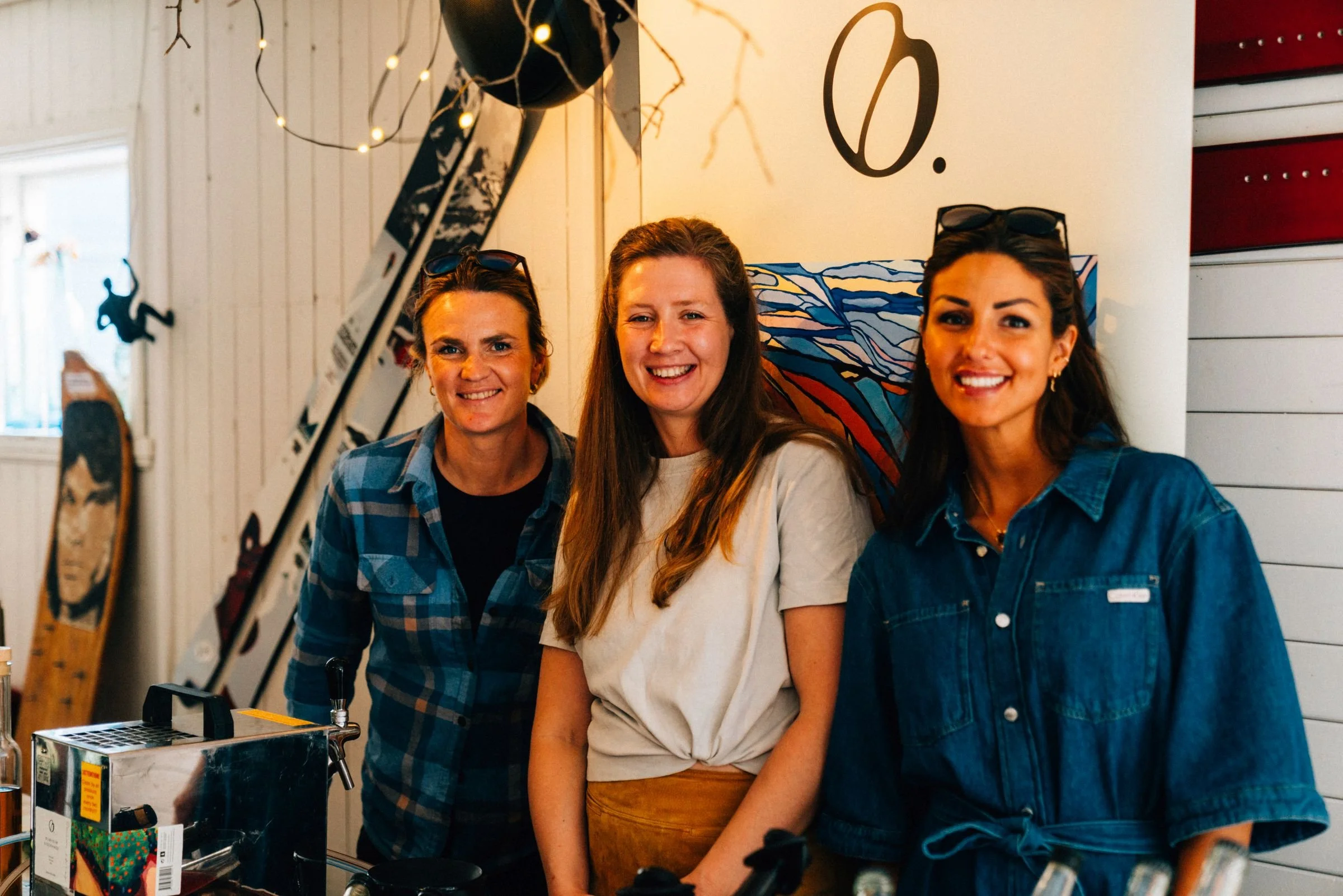 Tre kvinner som smiler og står foran en hvit vegg med dekorasjoner.