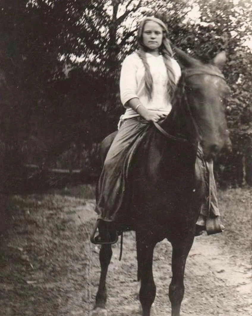 A girl with long braided hair riding a horse outdoors.