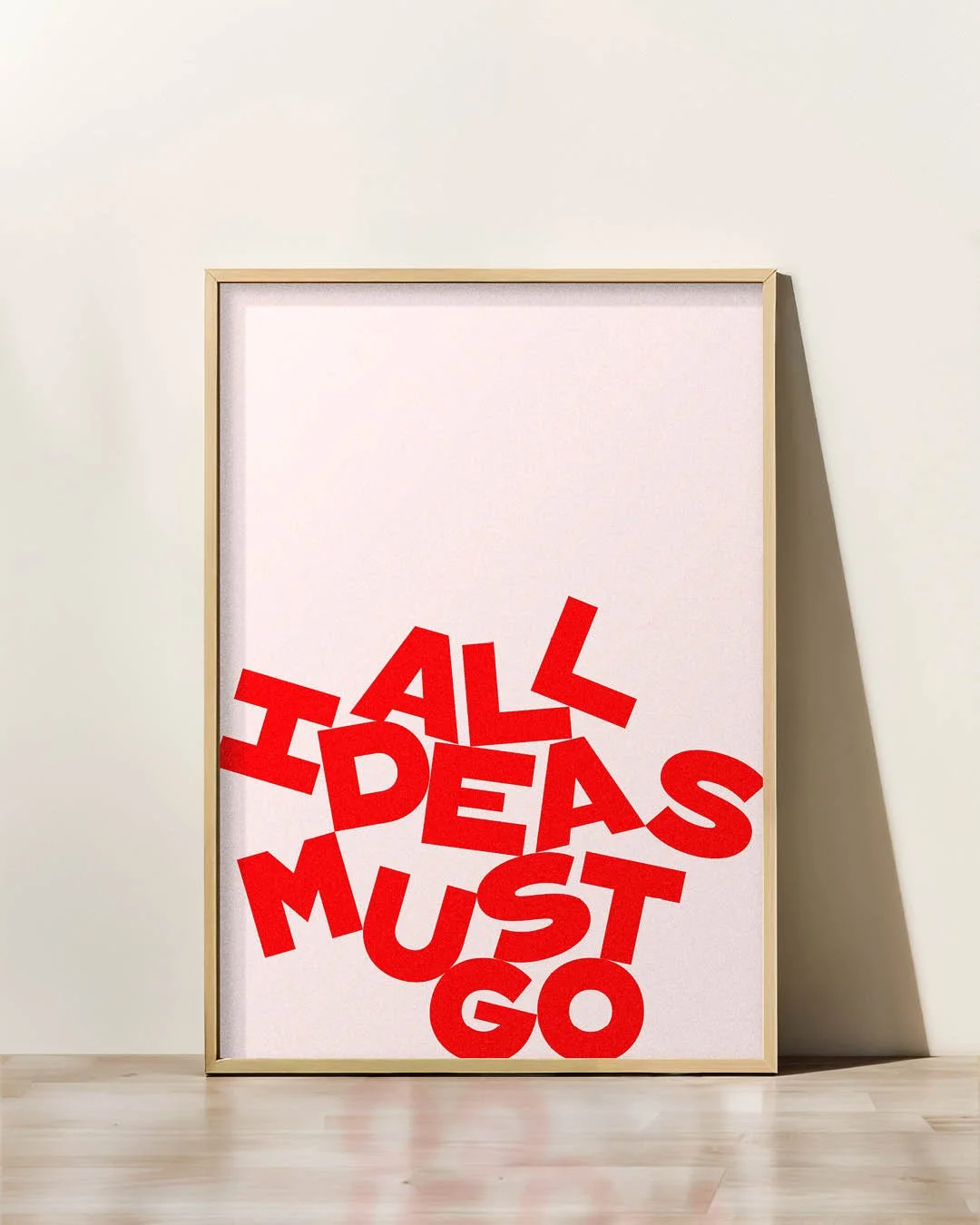 Framed poster with the phrase "ALL IDEAS MUST GO" in bold, jumbled red letters against a pale pink background.