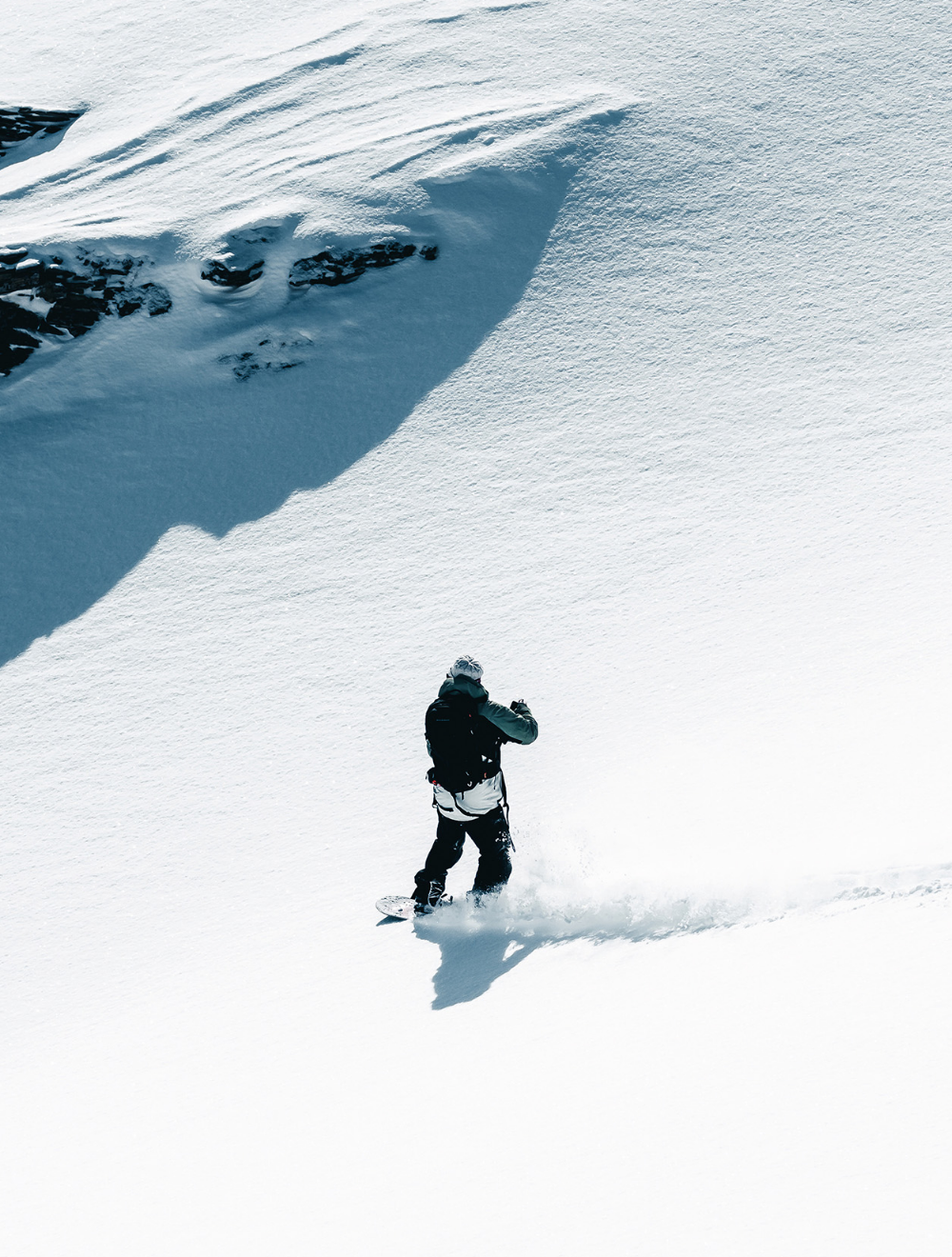 A person snowboarding on a snowy mountain slope with a large snow-covered rock or cliff in the background