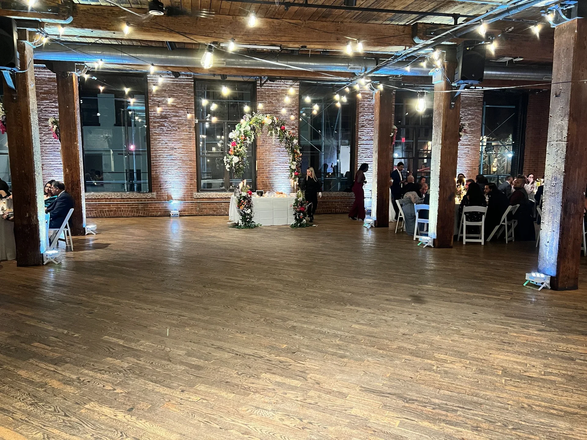 Wedding reception setup at Dumbo Loft in NYC with elegant uplighting, floral arch, and Aria Melody DJ creating a modern event atmosphere.