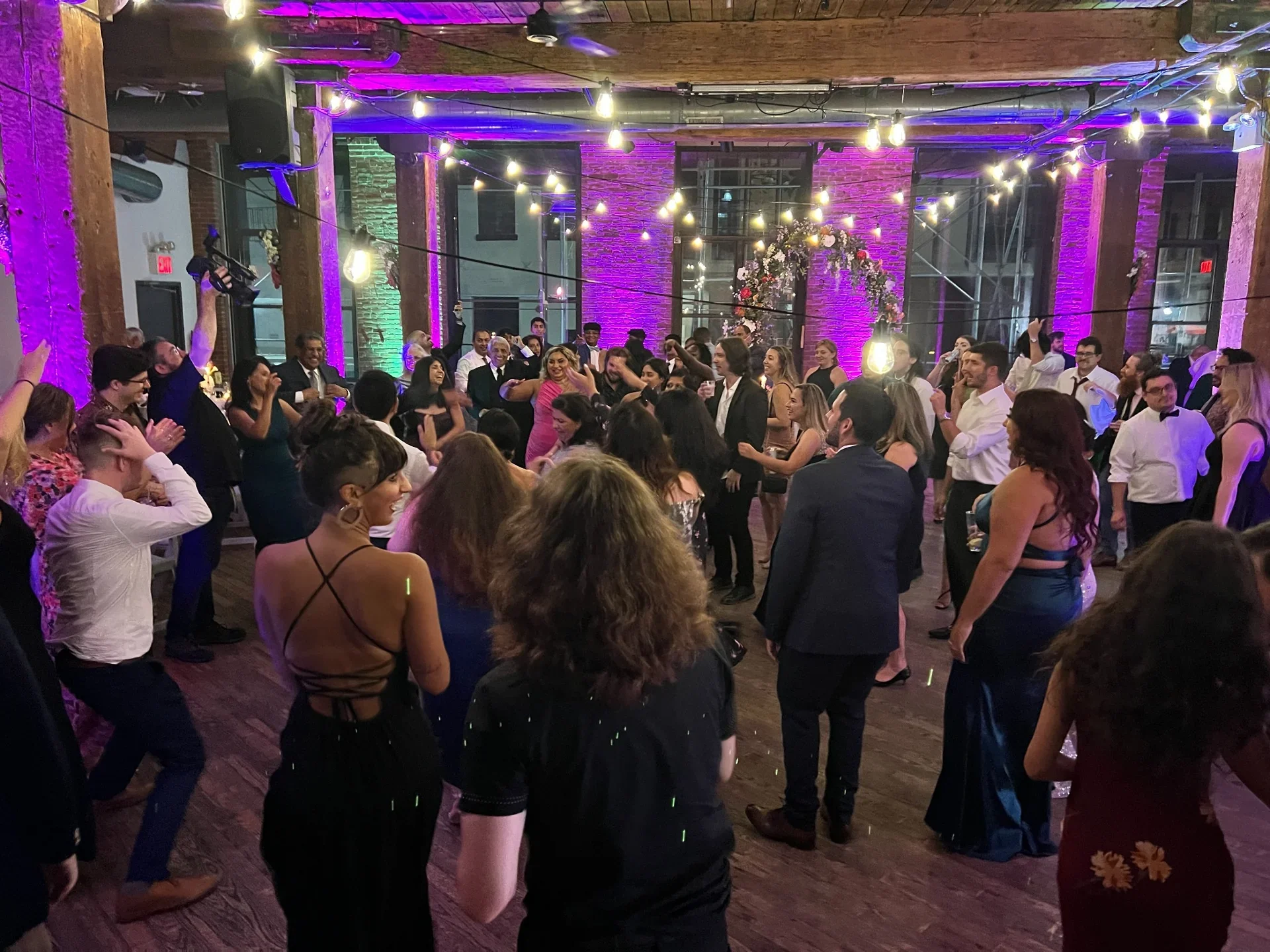 Wedding guests dancing under vibrant uplighting at Dumbo Loft in NYC, with Aria Melody DJ keeping the dance floor full all night.