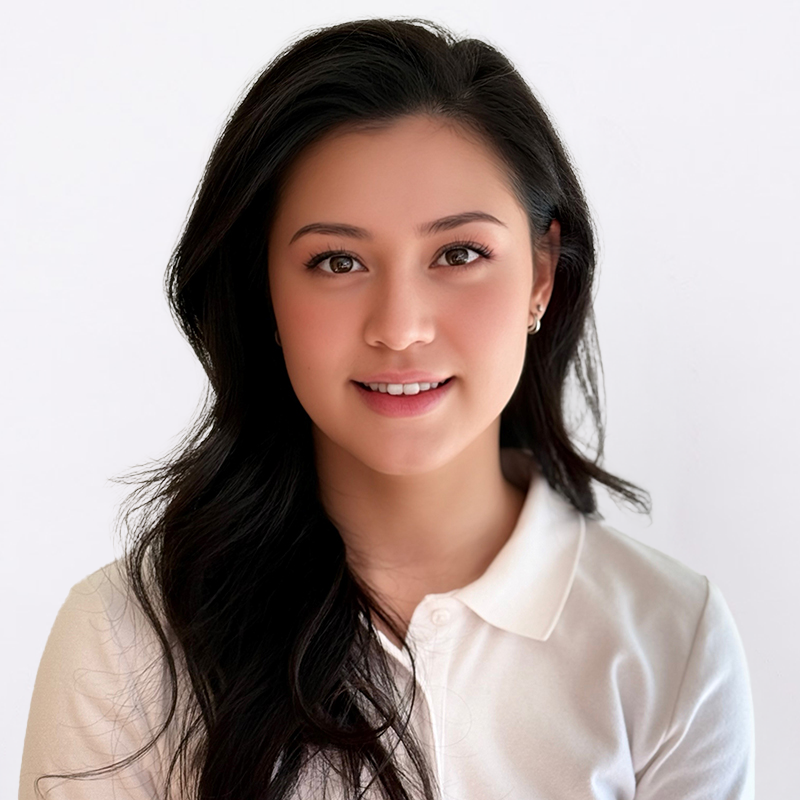 Portrait of a young woman with long dark hair, wearing a white collared shirt, smiling at the camera against a plain white background.