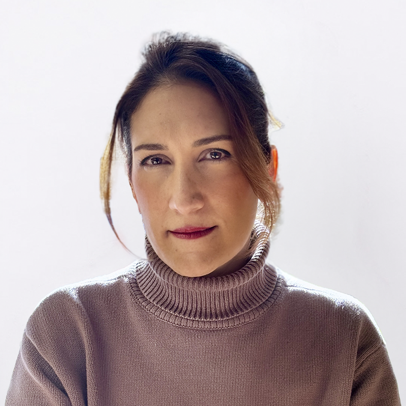 A woman with brown hair in a bun wearing a beige turtleneck sweater, looking at the camera with a slight smile against a plain light background.