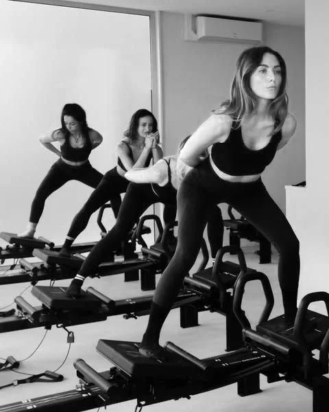 Three women in athletic wear exercising on Pilates reformer machines in a gym.
