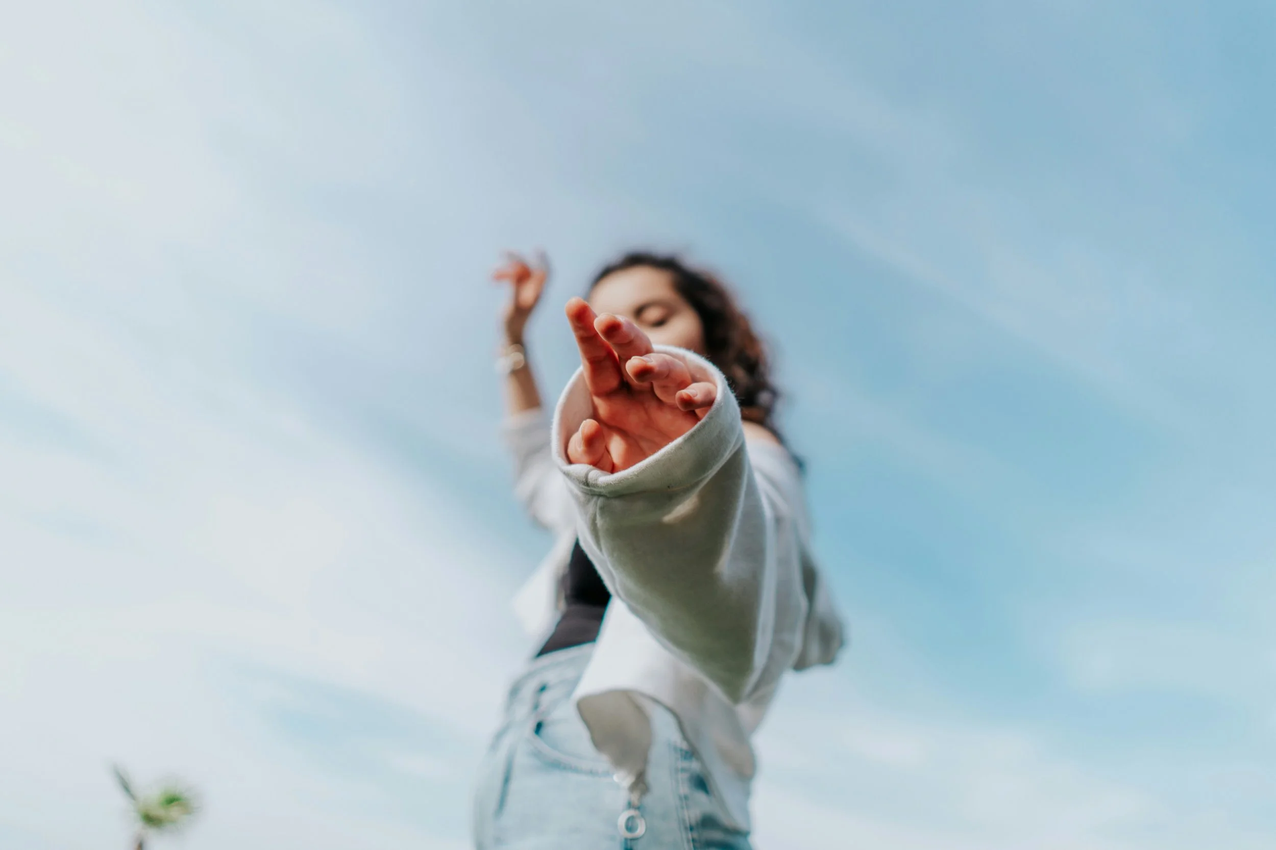 A woman reaching out towards the camera with her hand, standing outside under a blue sky.