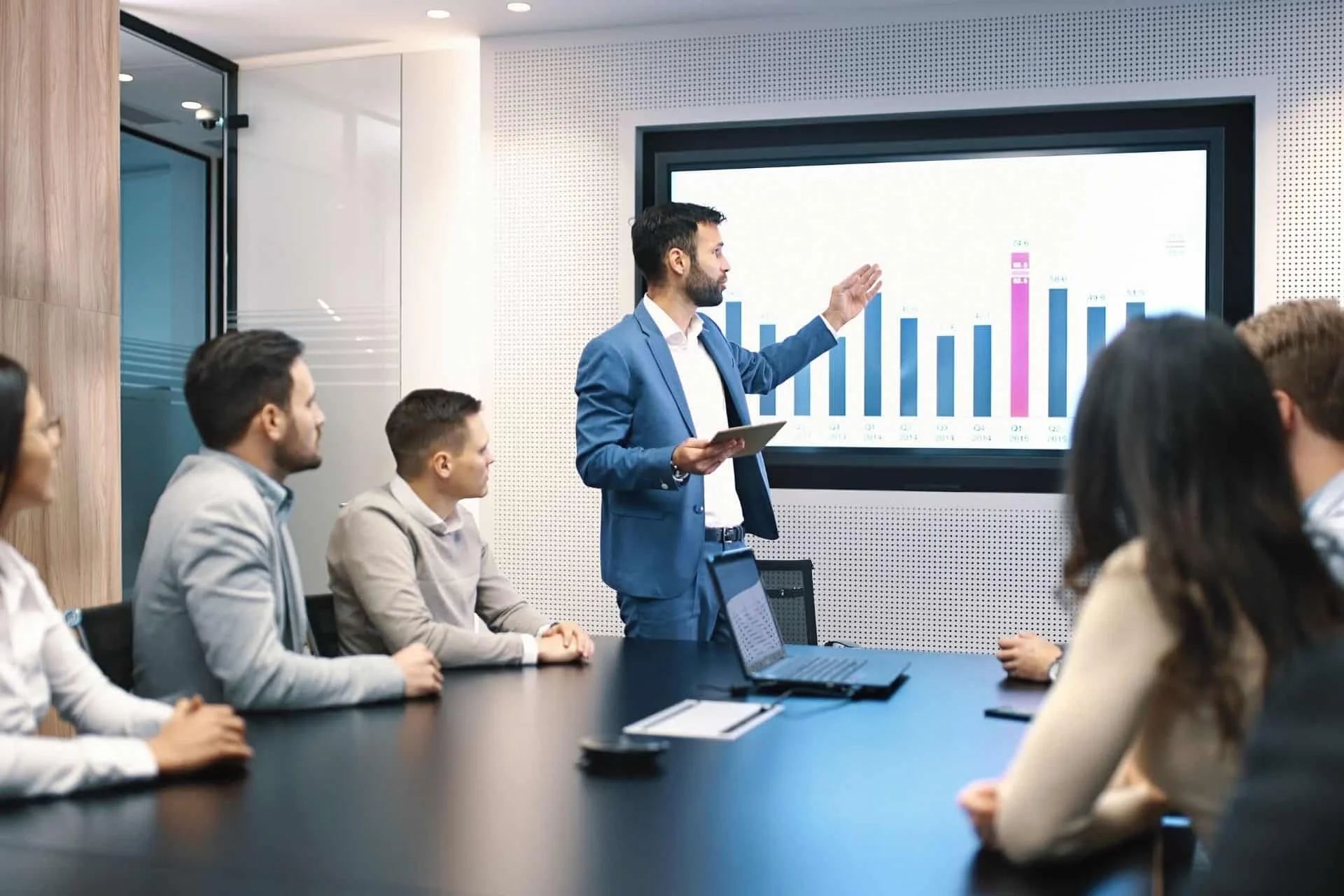 Boardroom meeting with a man reviewing a graph on a screen in front of others