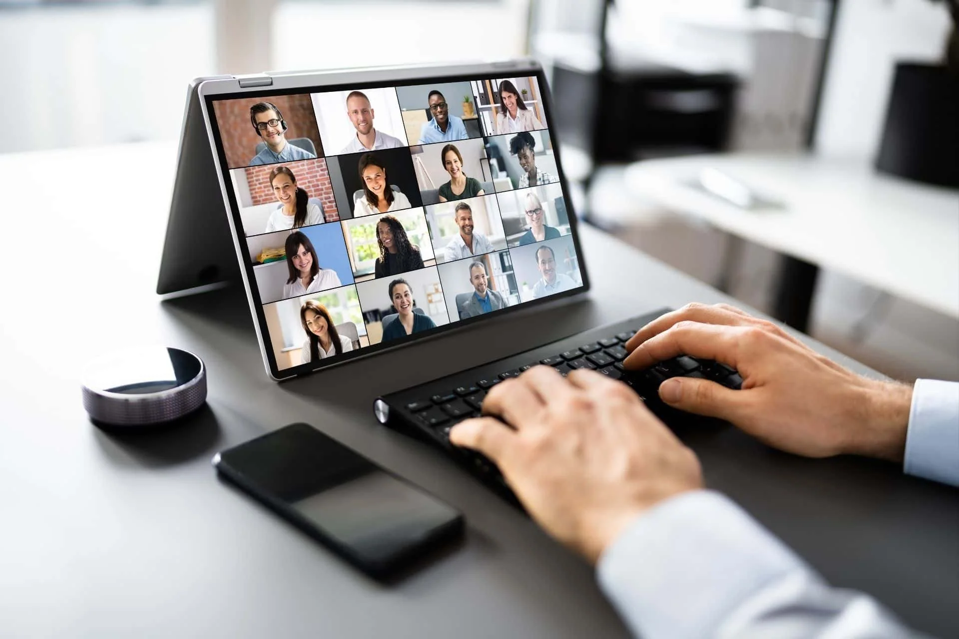 a person at a keyboard on a zoom call with multiple participants on screen