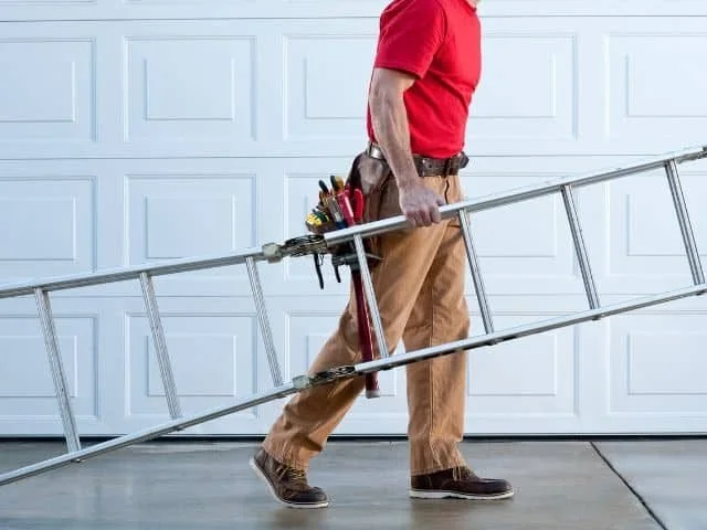 A person holding a ladder and a tool belt with various tools, standing in front of a white garage door.