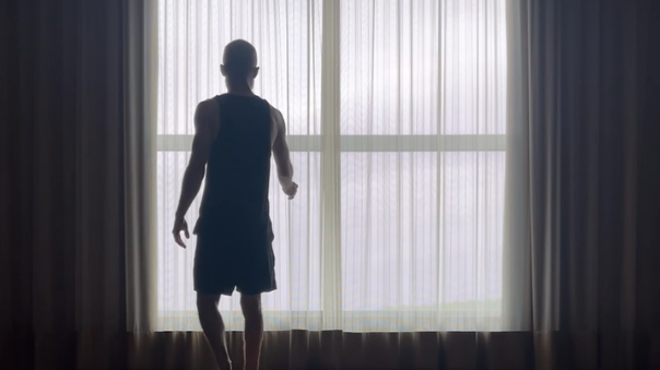 A man standing in front of a large window with sheer curtains, looking outside of the yoga studio.
