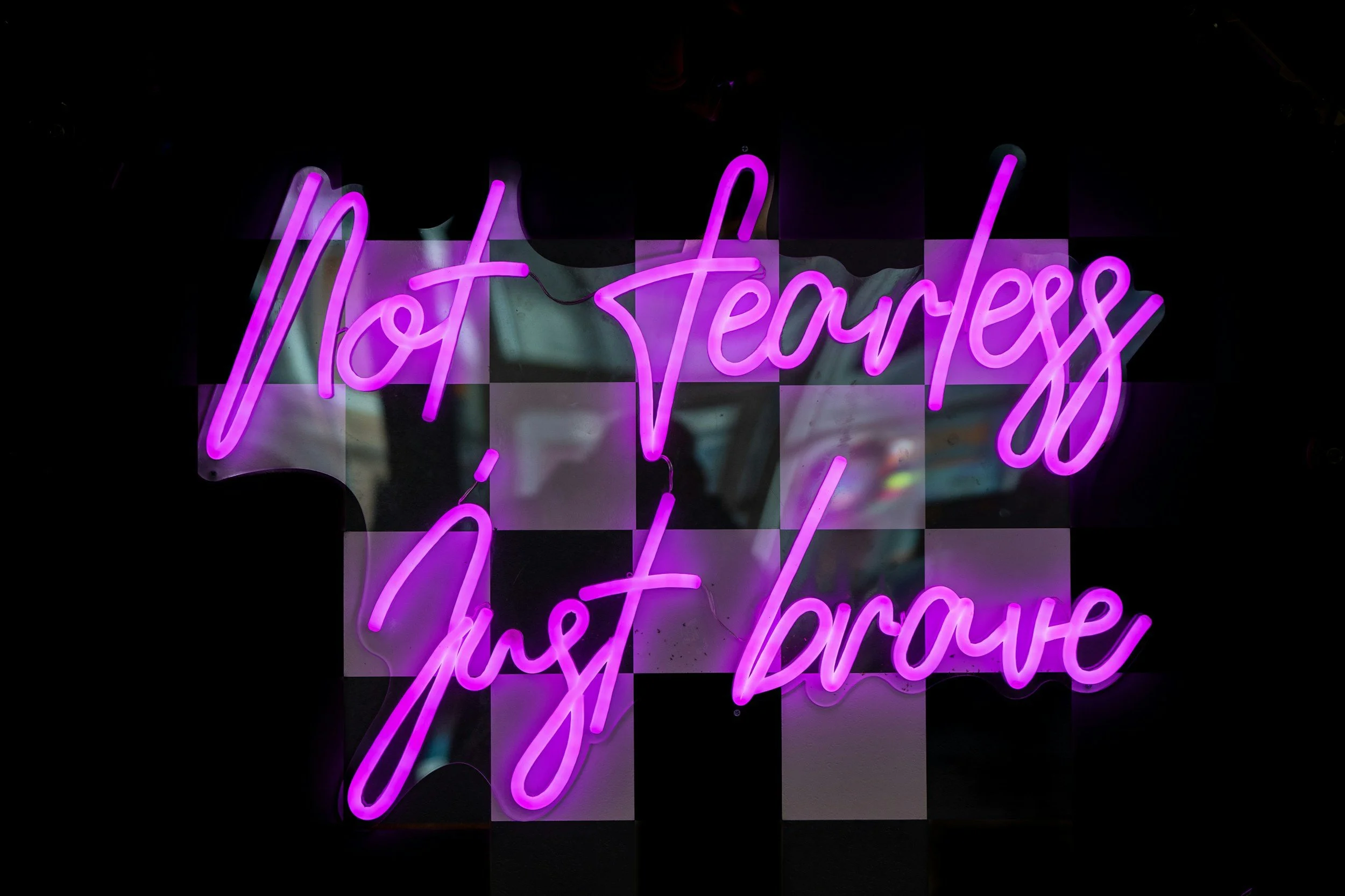 An image of a neon sign which says, "Not fearless, Just Brave."