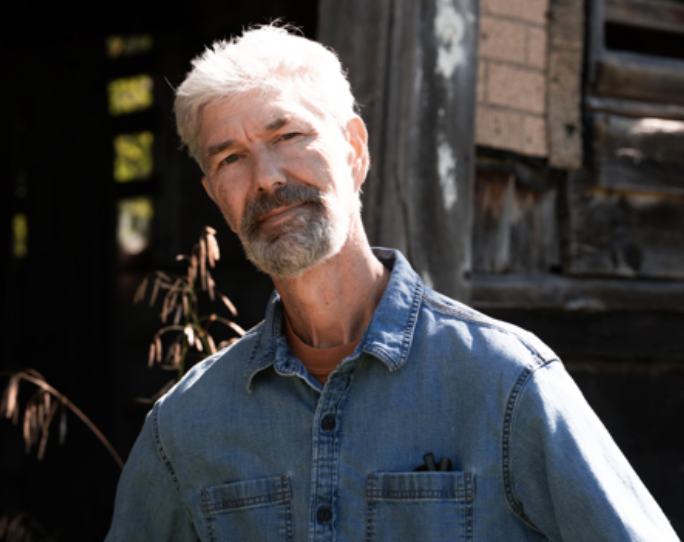 Doug Kolmar in a blue button down work shirt looks compassionately and openly towards the camera.