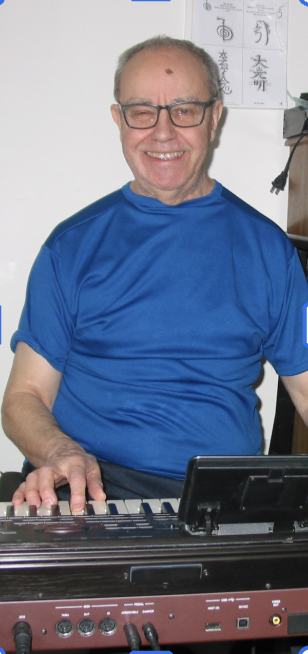 Patrick sits at a keyboard in a bright blue shirt beaming at the camera.