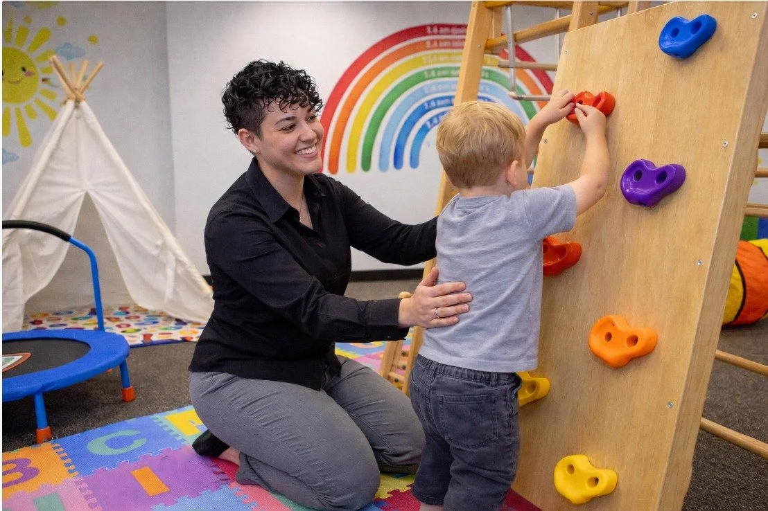 Child participating in individualized, play-based learning activities with a therapist in a colorful early childhood education center, featuring a rainbow mural that supports cognitive, social, and emotional development;