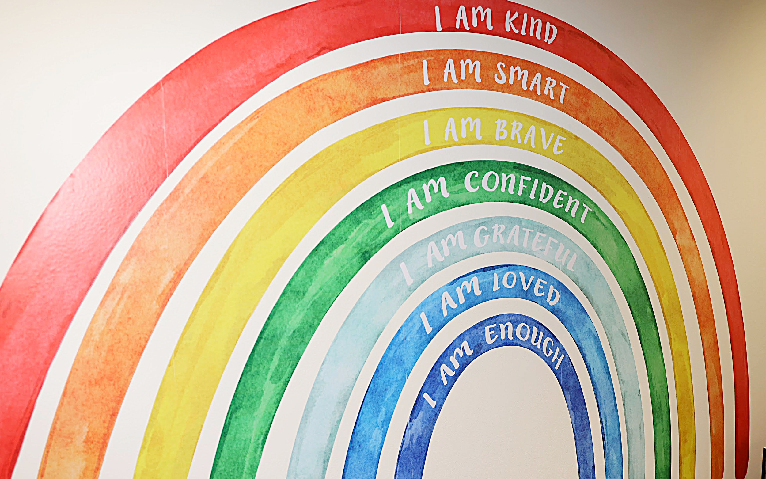 Colorful rainbow mural with positive affirmations in white text, including 'I AM ENOUGH,' 'I AM LOVED,' 'I AM GRATEFUL,' 'I AM CONFIDENT,' 'I AM BRAVE,' 'I AM SMART,' and 'I AM KIND'.