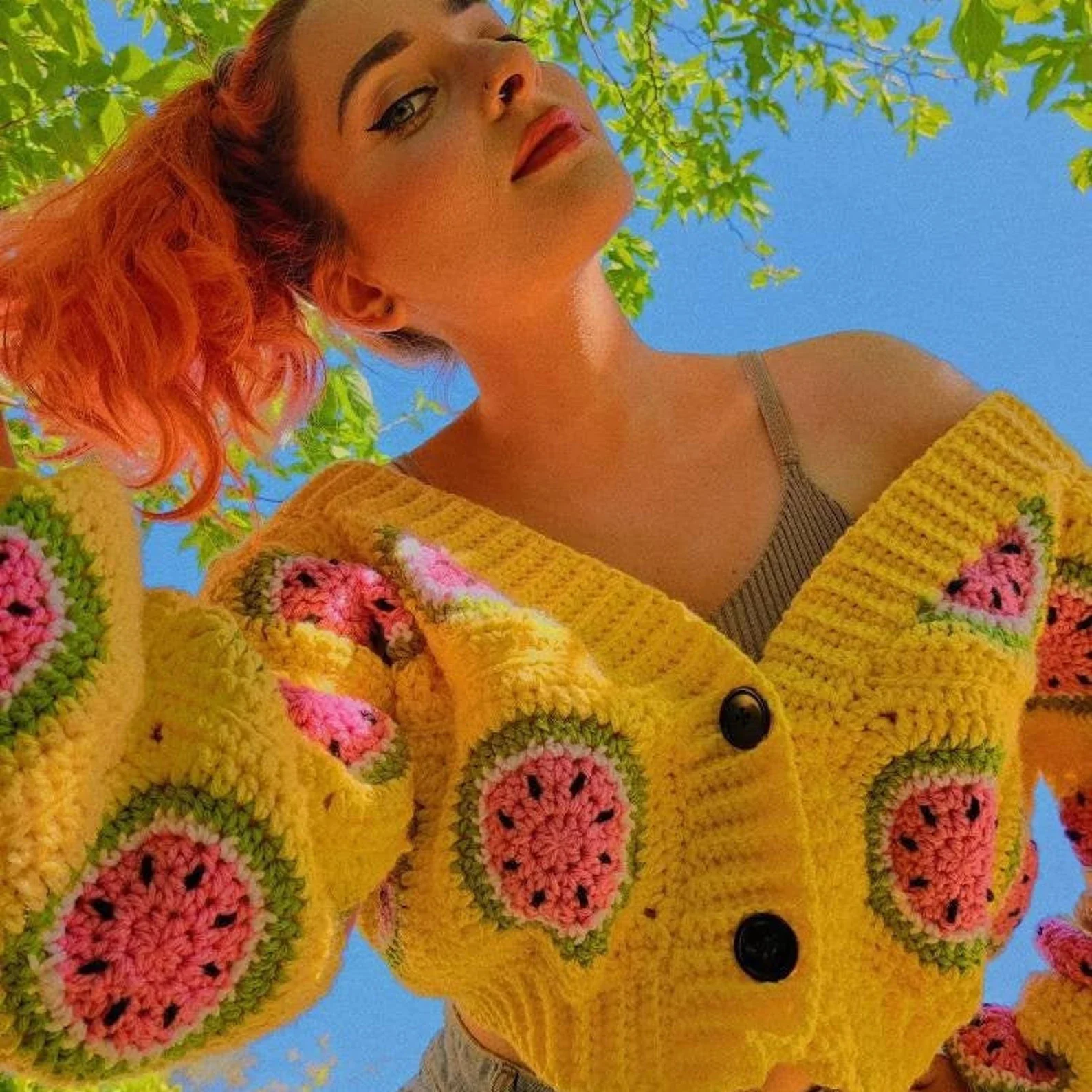 Cropped watermelon granny square crocheted cardigan. Bright yellow with watermelon motifs, ribbed hem and button bands and two large brown buttons. Off shoulder, v-neck style.