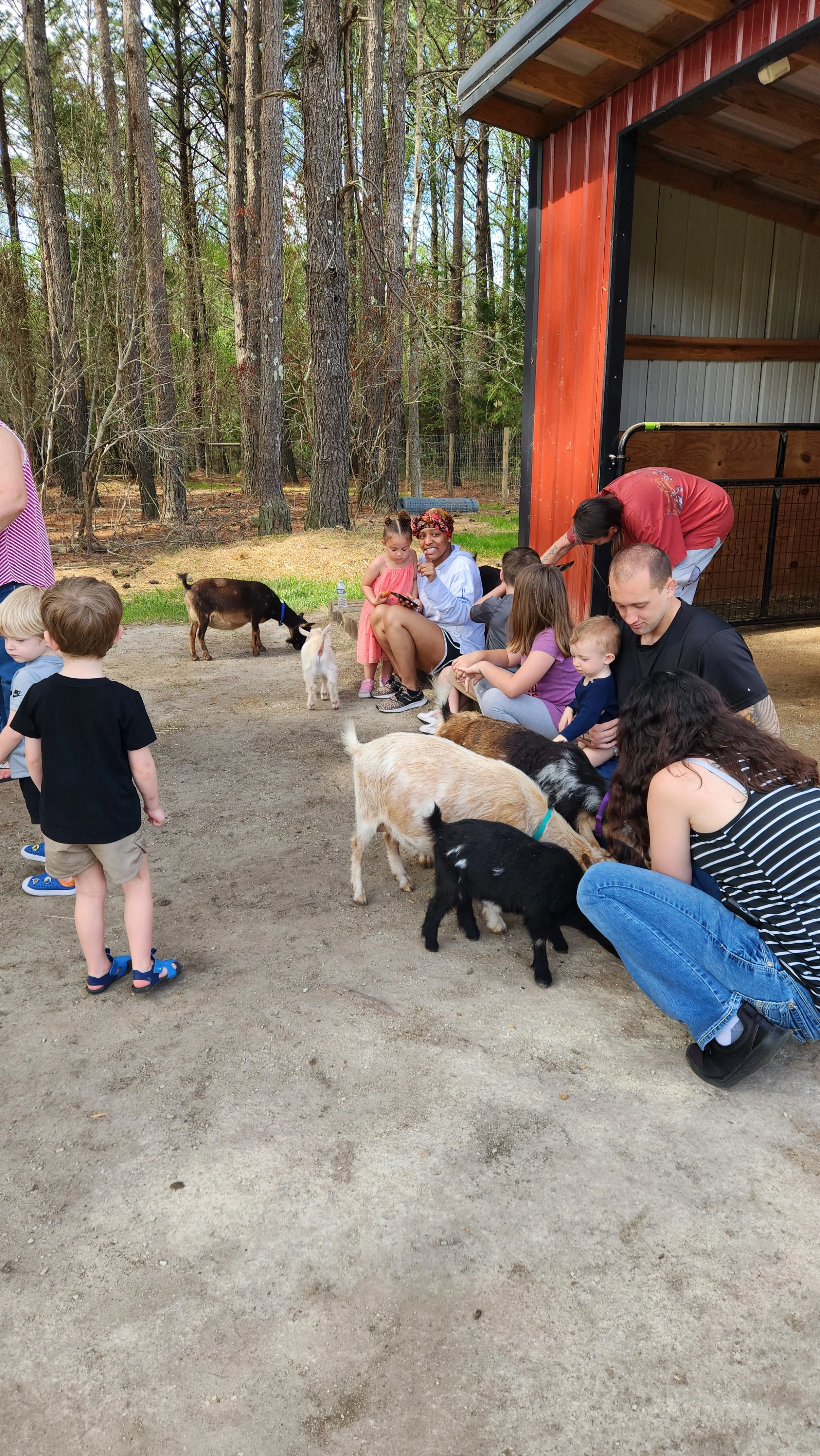 Children and adults petting goats at a farm.
