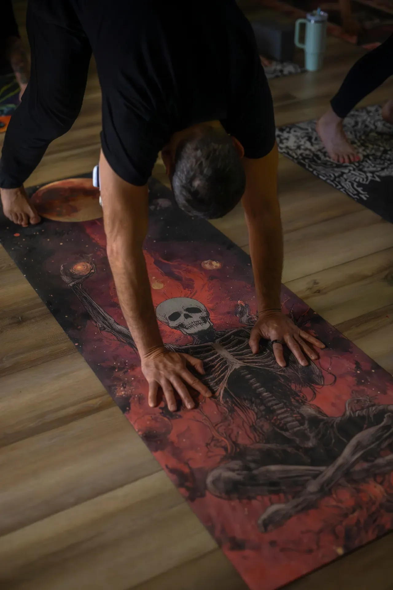 A man in downward dog yoga pose on a metal-inspired mat displaying a skeleton and moon