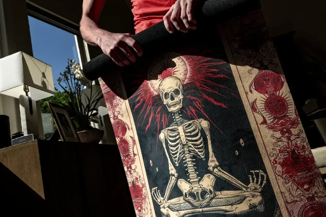 a man rolls up a yoga mat that depicts a metal-inspired skeleton and sun
