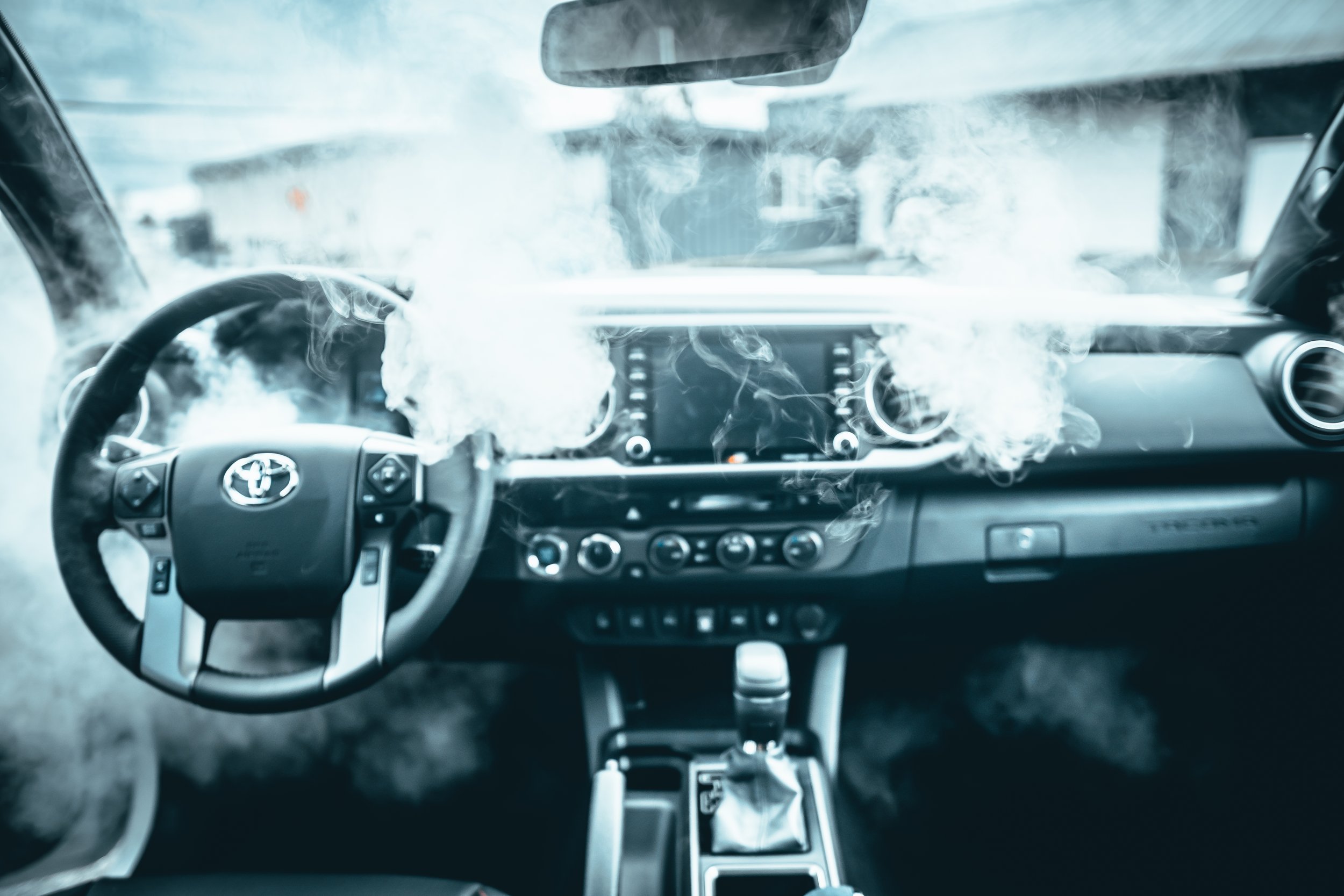 The interior of a car with smoke coming out from the dashboard area.