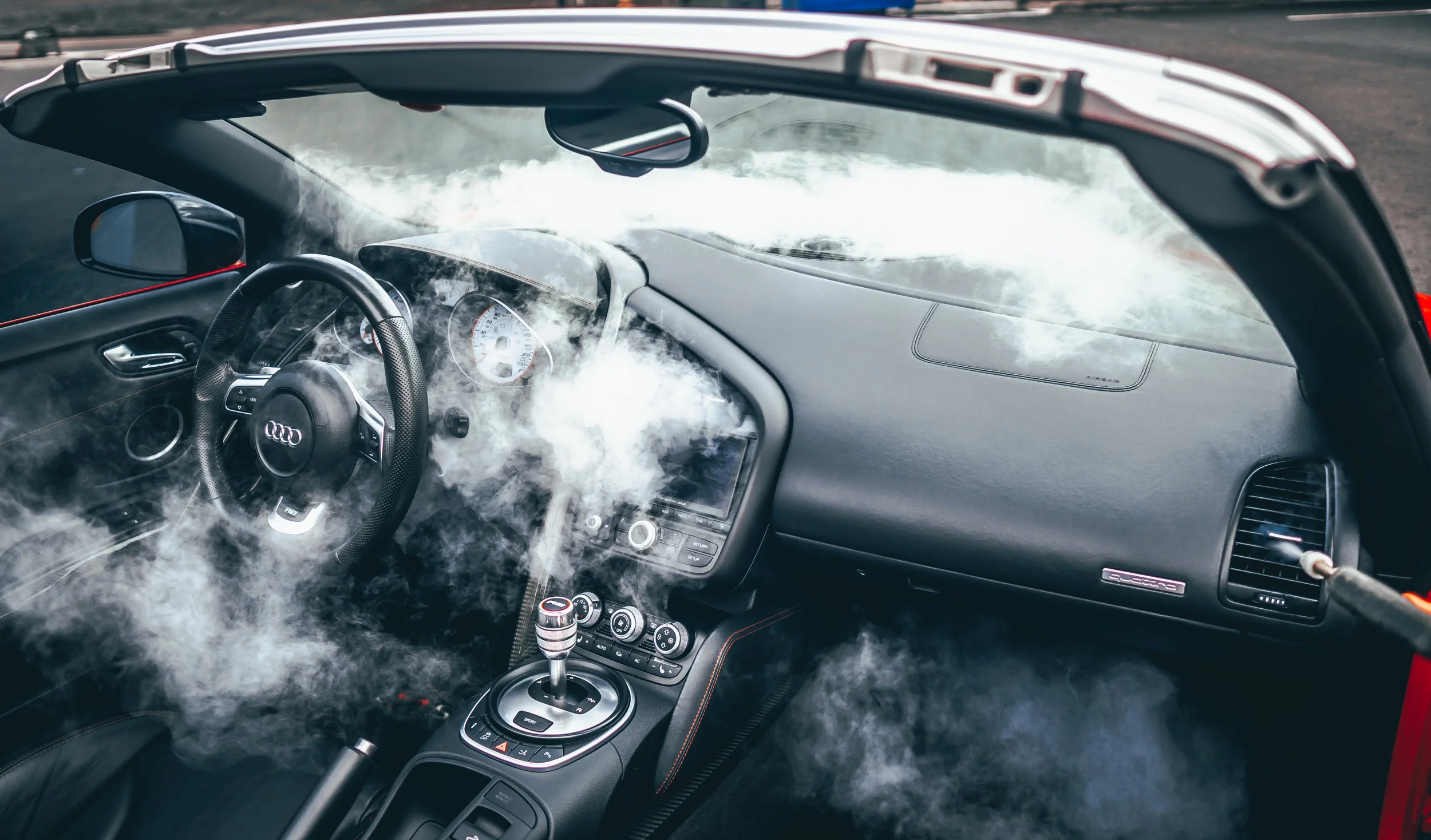The interior of a red convertible sports car with smoke inside, including a steering wheel with an Audi logo, dashboard, and center console.