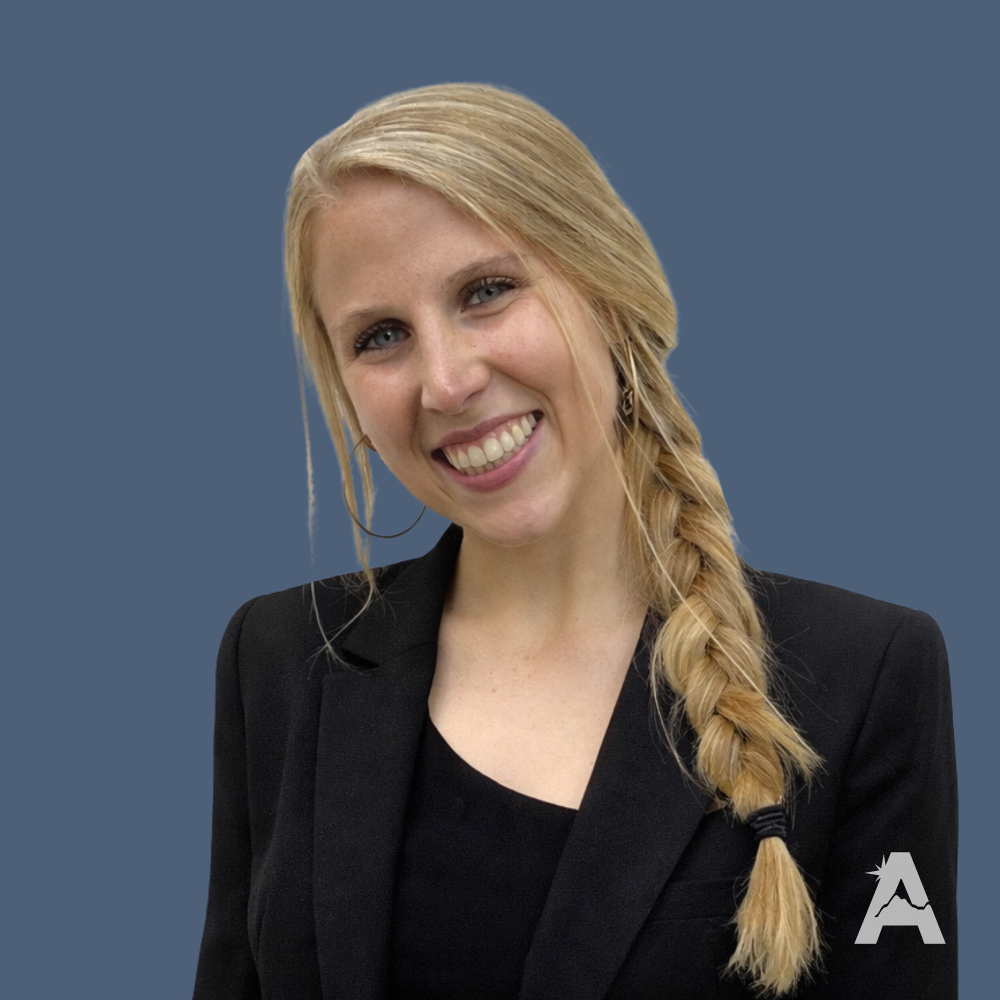 A young woman with blonde hair in a loose braid, wearing a black sleeveless top, smiling and standing against a white textured wall.