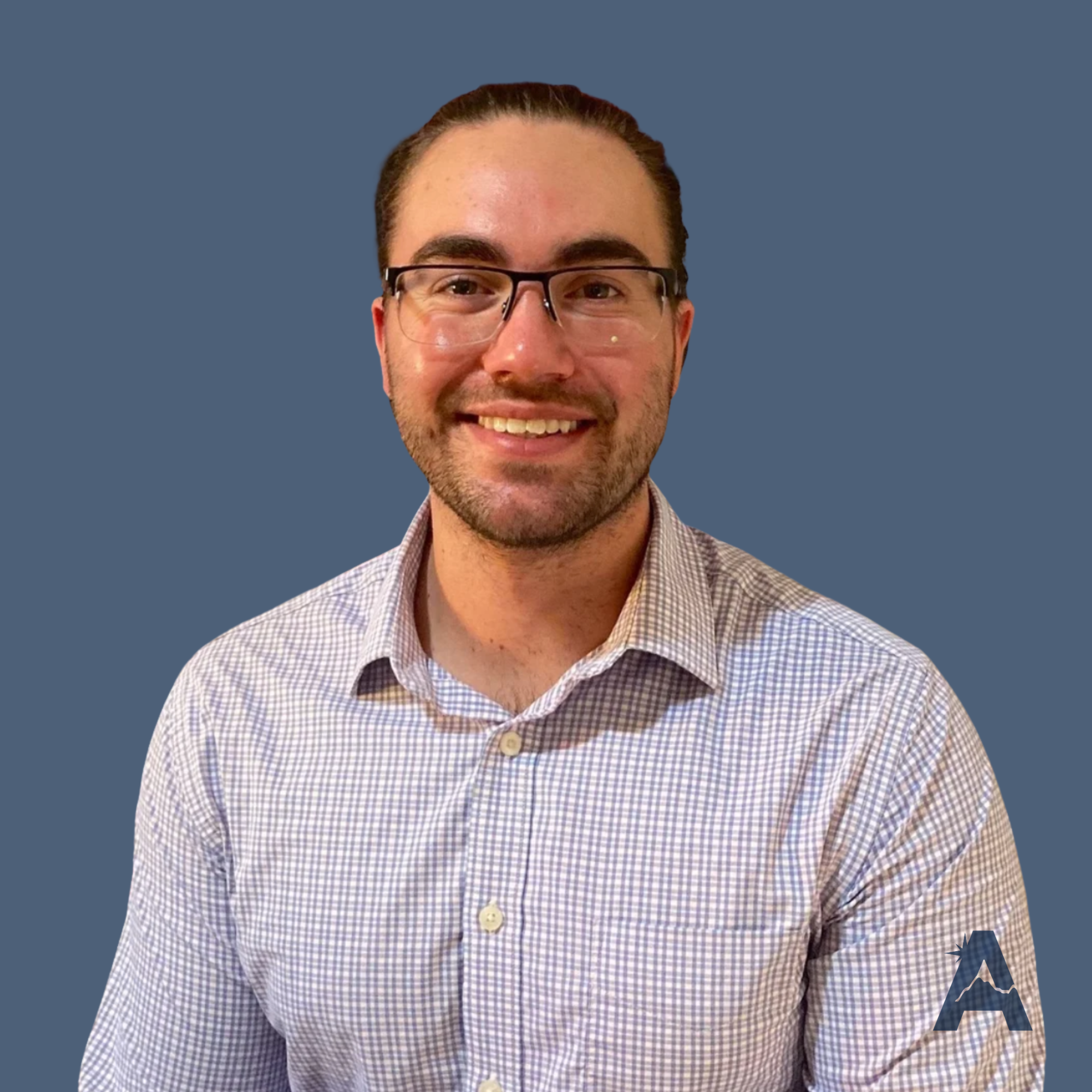 A portrait of a man with glasses, smiling, wearing a checkered button-up shirt, with a blue background and a logo featuring a stylized letter 'A' in the lower right corner.