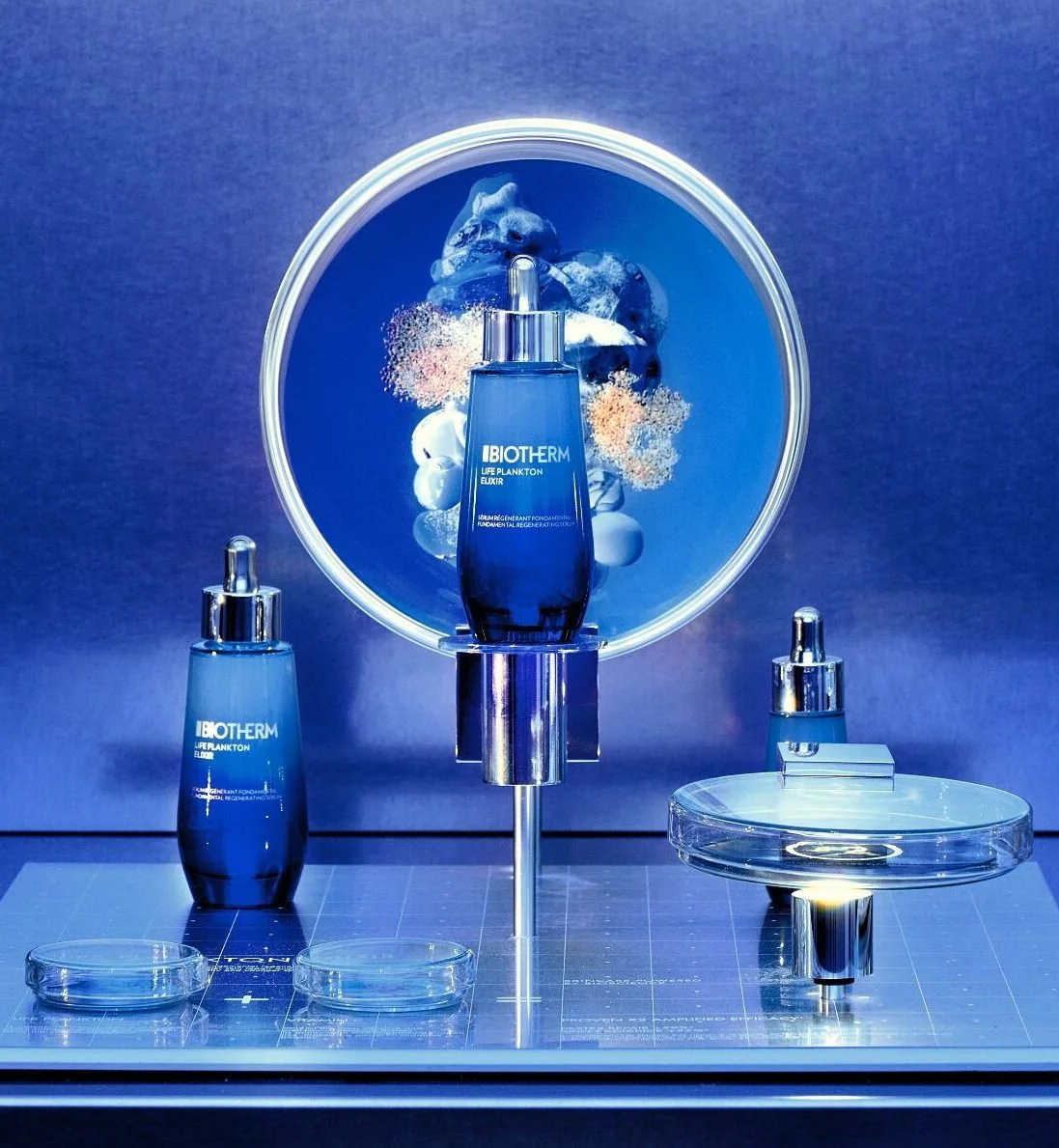 Display of blue skincare bottles labeled IBIOTHERM Life Plankton Elixir on a reflective surface with a glowing circular background.