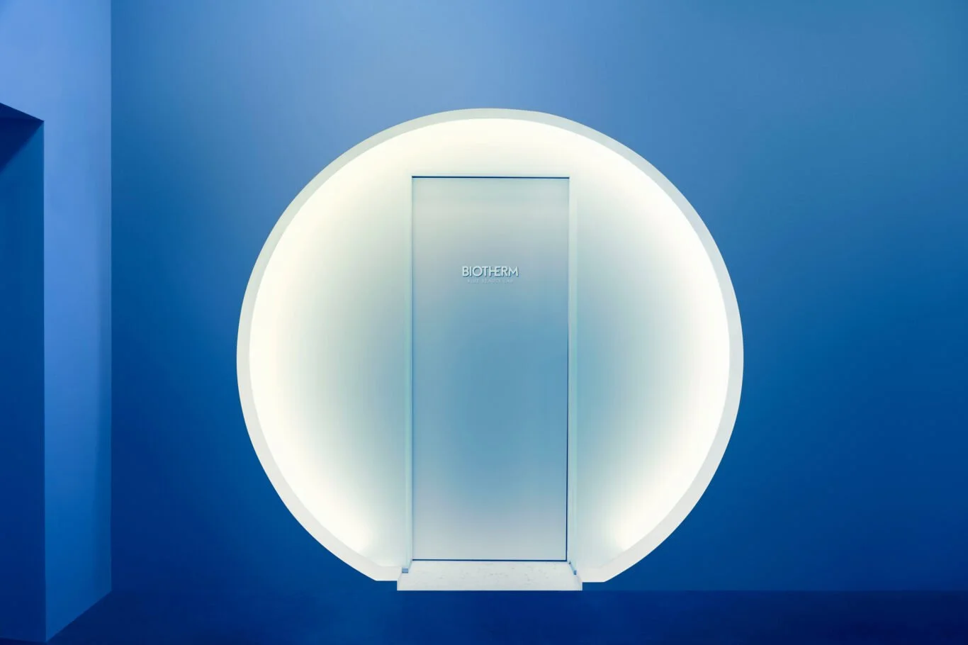 Frosted glass door in a blue room with the word "BIOTHERM" on it, set within a circular lighted frame.