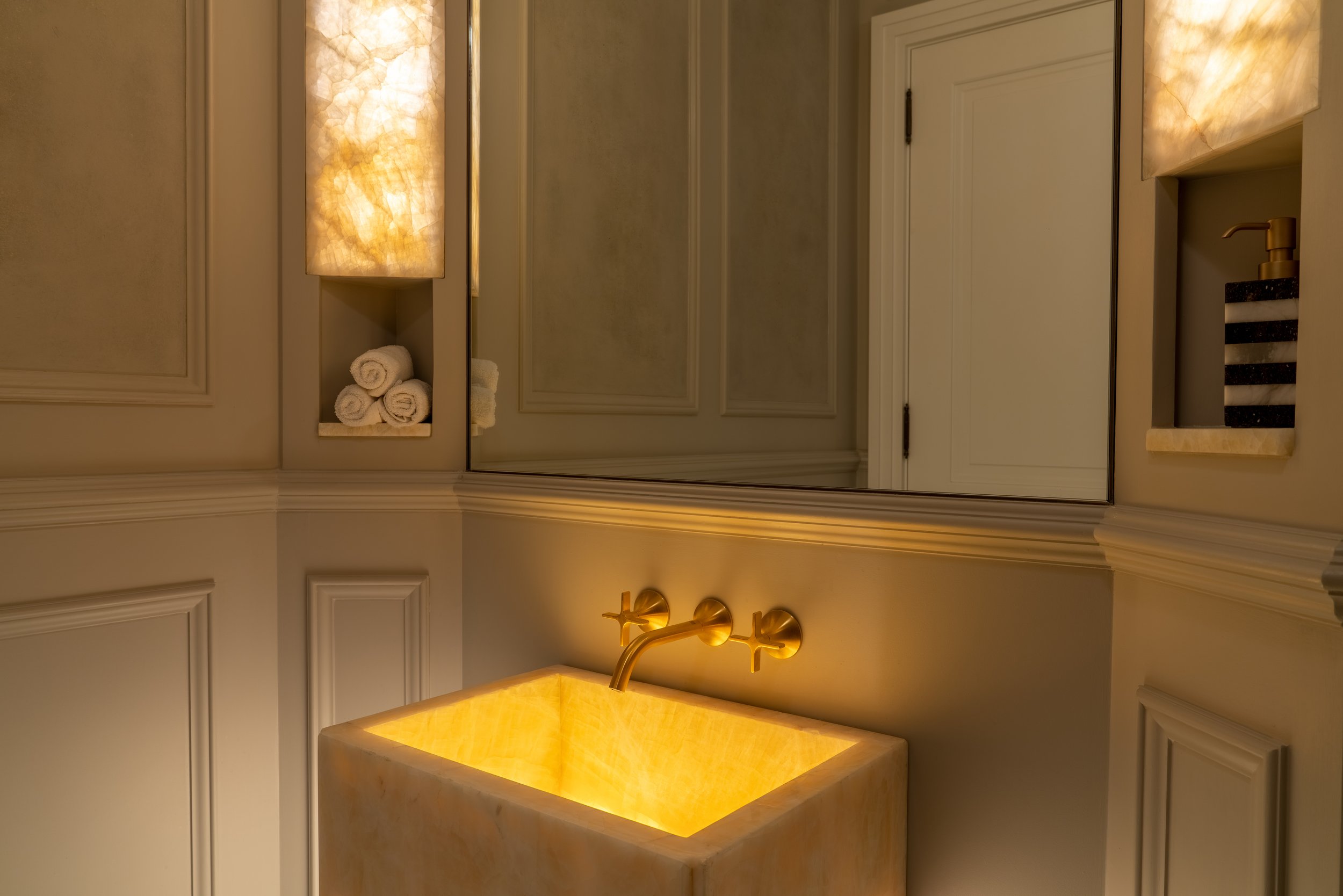 Luxurious bathroom with illuminated basin, gold fixtures, and ambient lighting.