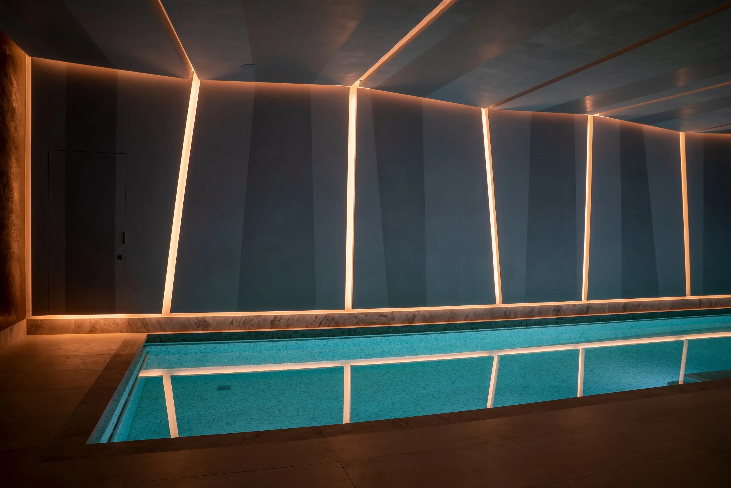 Indoor swimming pool with illuminated wall panels in a modern, dimly lit room.