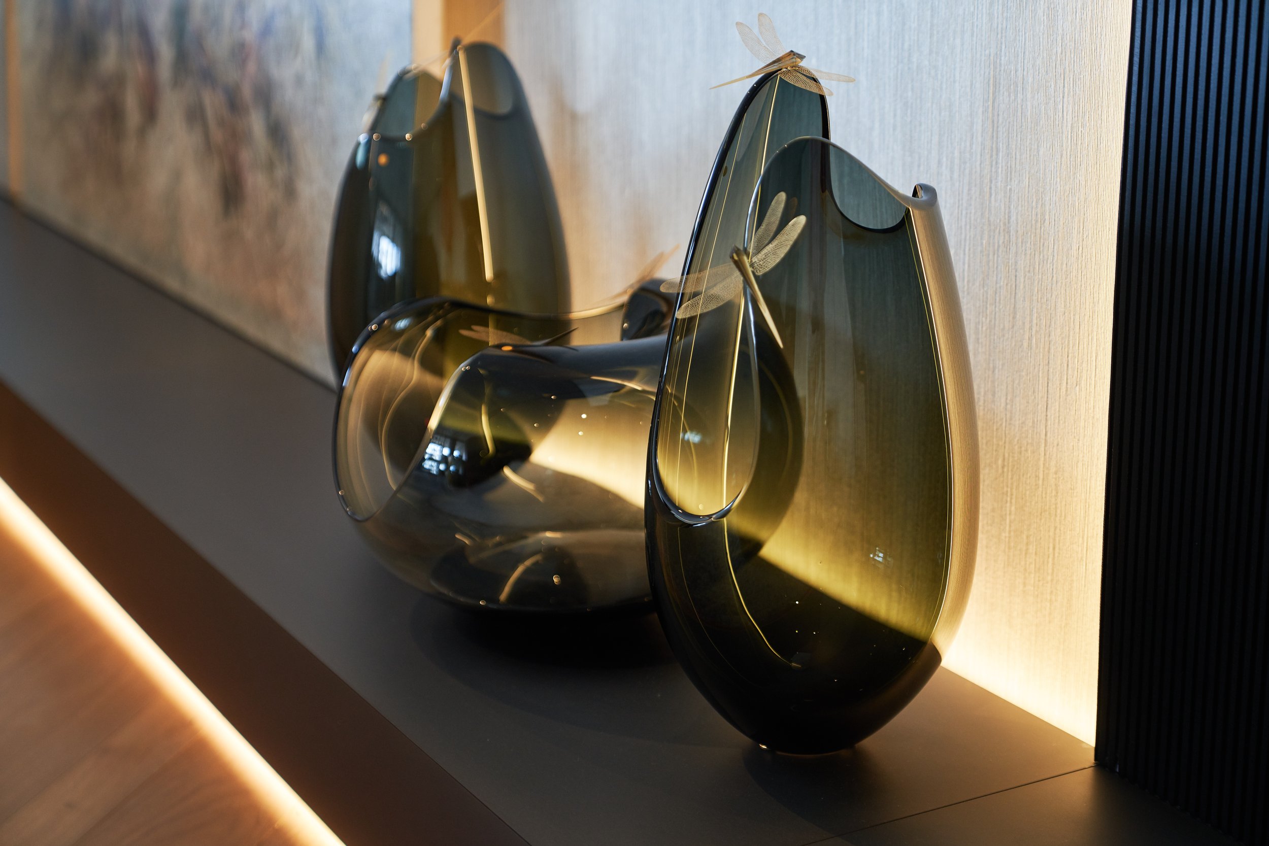 Three artistic glass vases with dragonfly adornments displayed on a wooden surface in a modern interior setting.