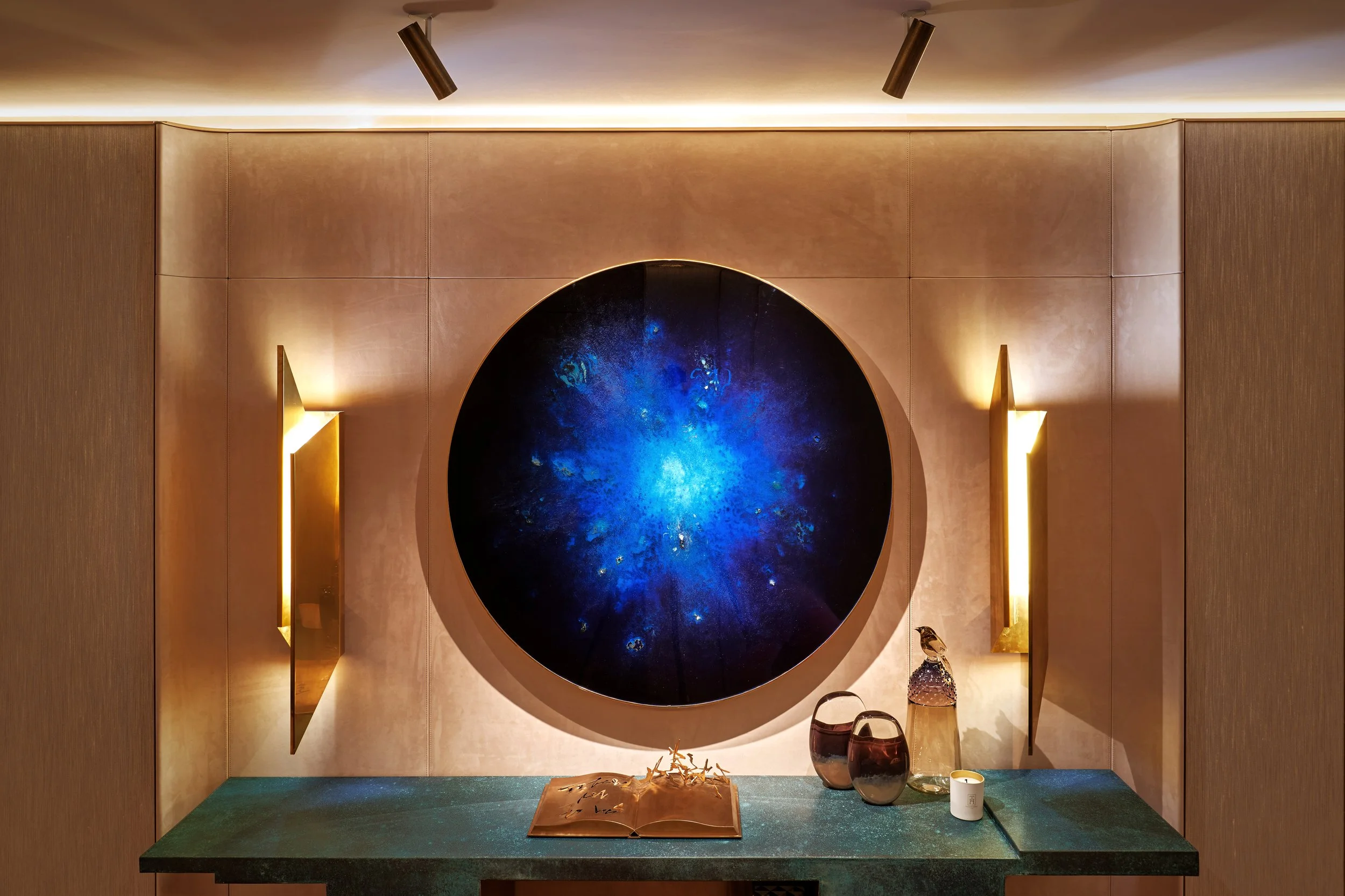 Elegant interior with a round blue artwork on wall, modern lighting, and decorative items on a green console table.