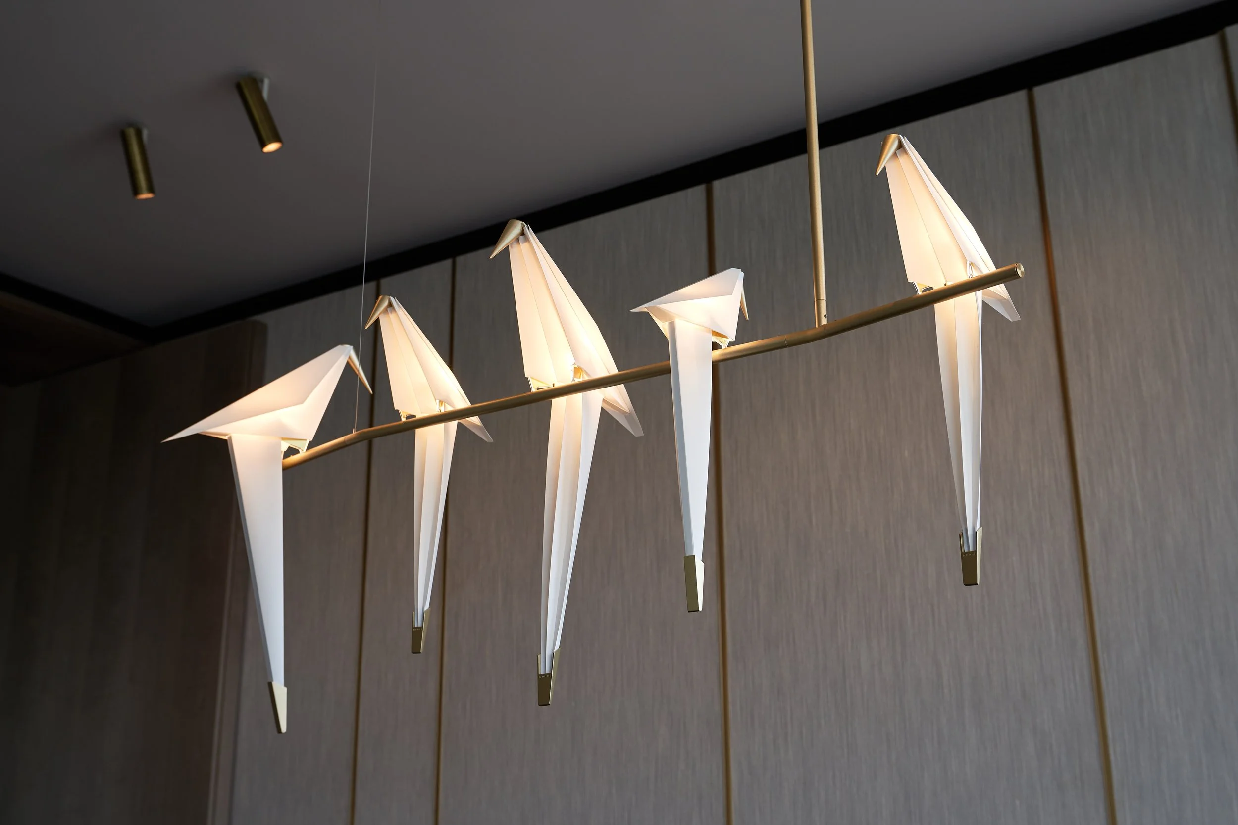 Modern chandelier with origami-style bird-shaped lights hanging from a metal rod in a room.