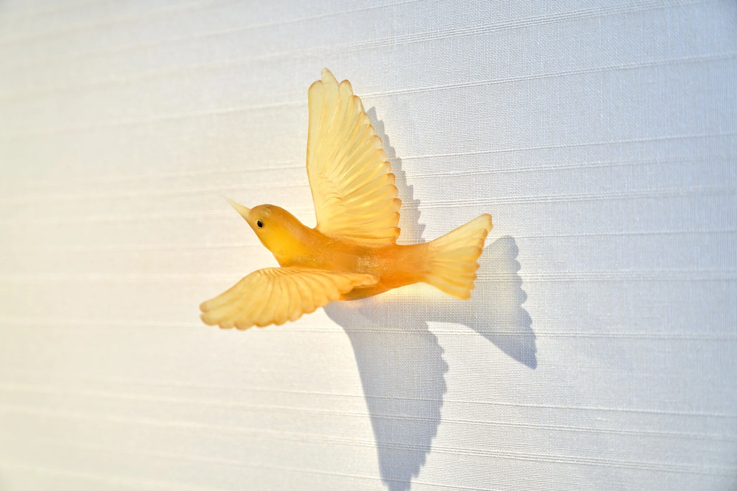 Yellow bird figurine casting shadow on a white textured surface.