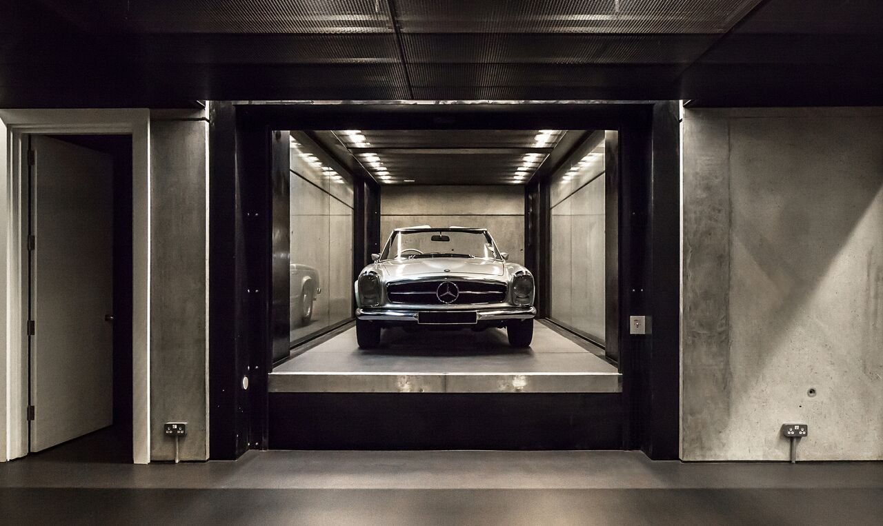 A vintage silver Mercedes-Benz car parked inside a modern, high-ceiling parking garage