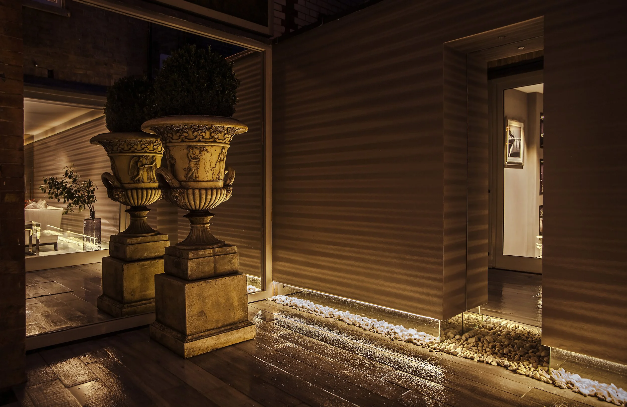 Elegant interior with two ornate stone planters holding bushes, decorative lighting, and a reflective wall panel.