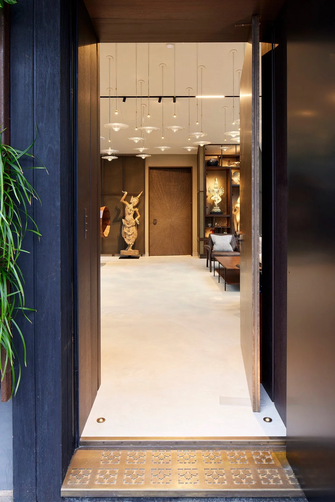View through open doorway into a modern, stylish interior space with sculptures, patterned shelving, seating, and decorative lighting.