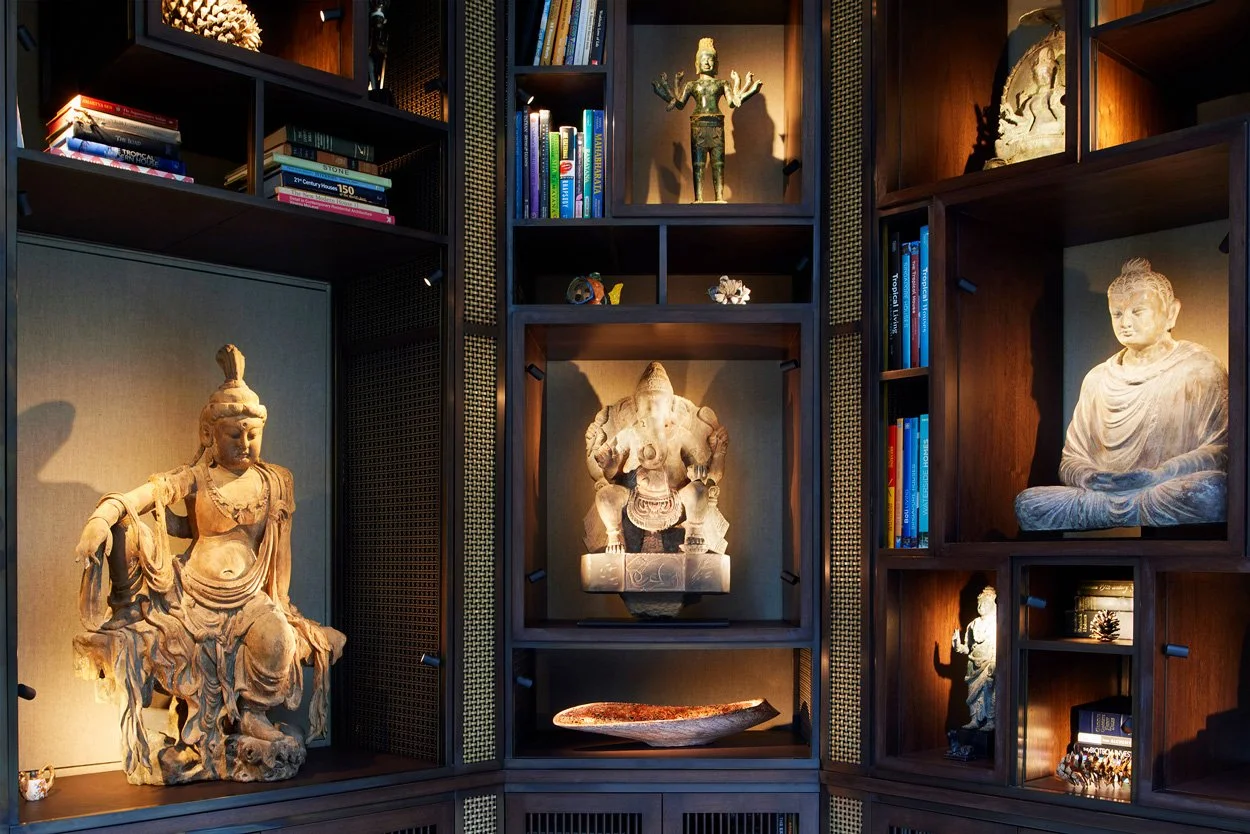 Bookcase with Asian statues and art objects, illuminated by warm lighting.