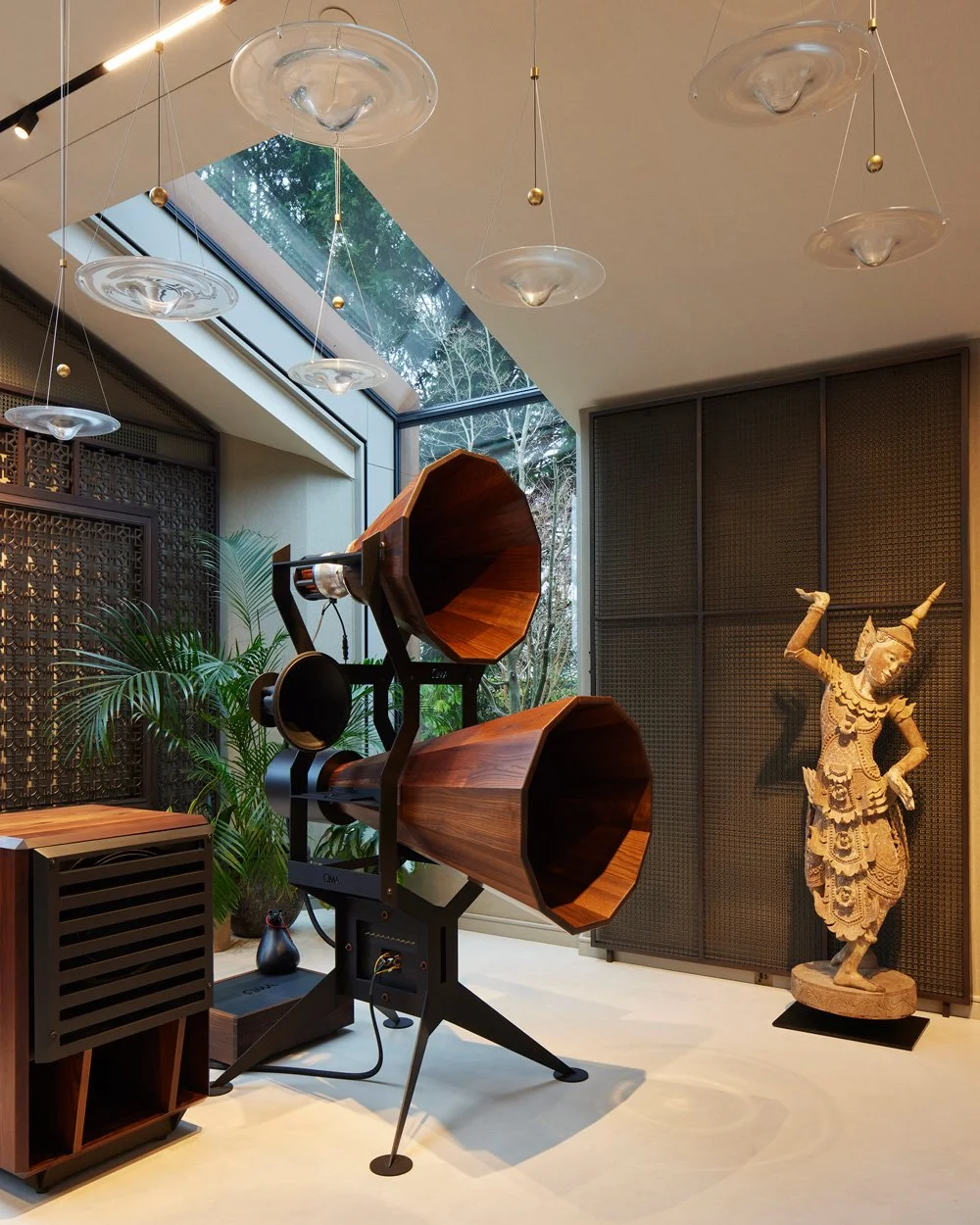 Interior room with a large, vintage wooden horn speaker, decorative sculpture of a dancer, plants, and modern ceiling lights, large skylight with natural light.