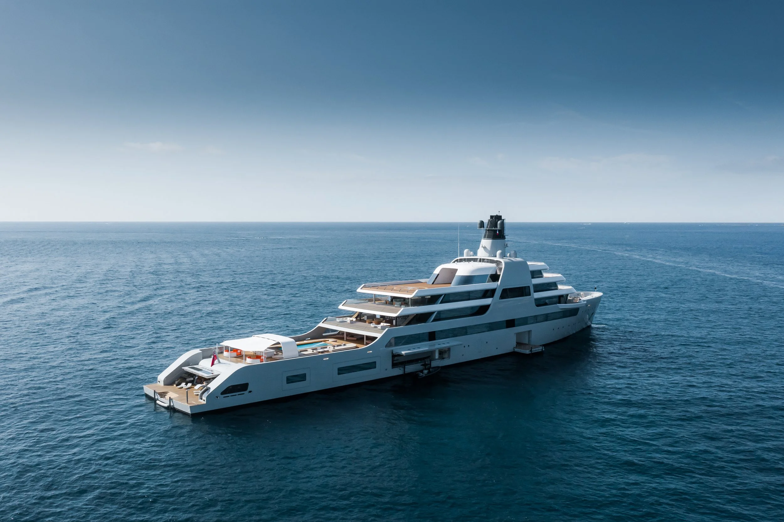 A large white luxury yacht sailing in calm blue ocean waters with a clear sky above.