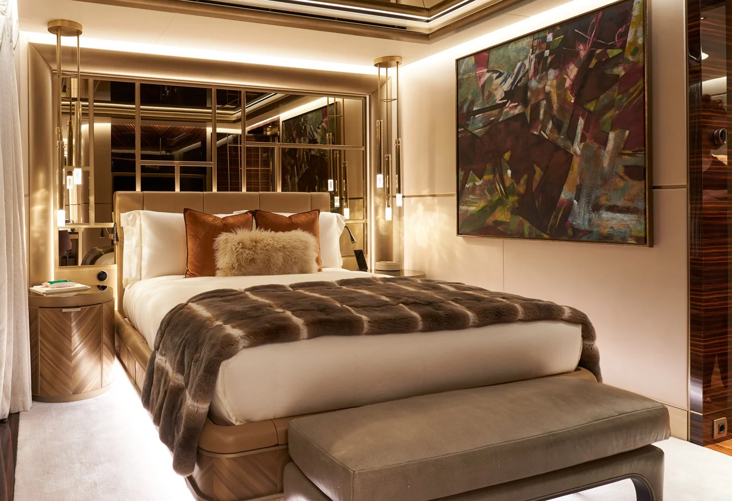 Luxurious hotel bedroom with a large bed, plush throw blanket, decorative pillows, modern lighting, abstract artwork, and mirrored wall panels.